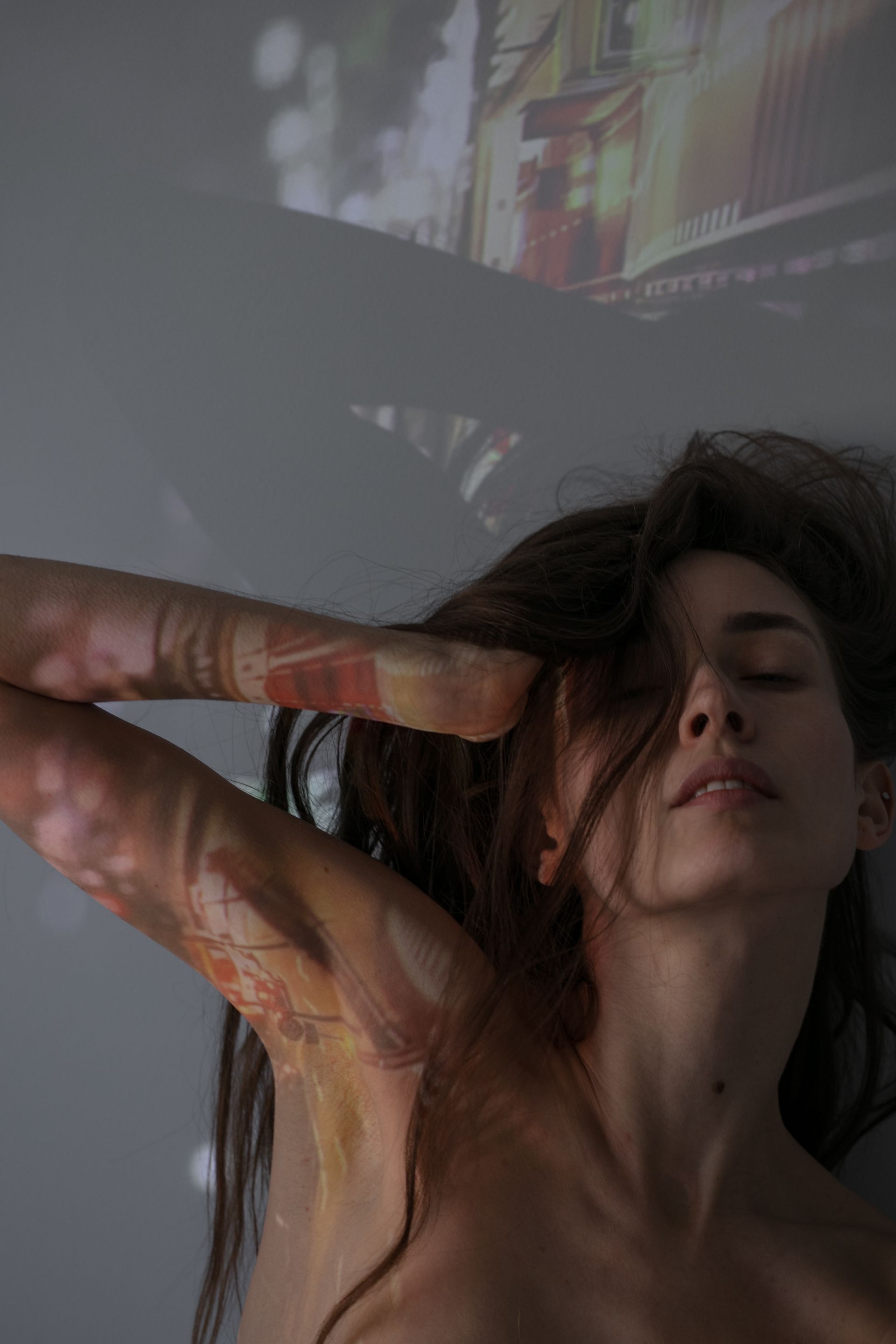 Woman with eyes closed, arm raised, with projected colorful images on arm and wall.