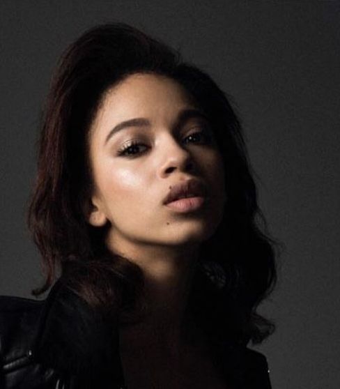 Woman with dark hair looking up with a neutral expression, wearing a black top, studio lighting.