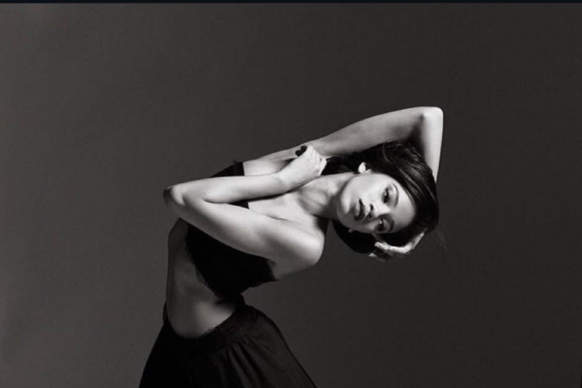 Woman in black outfit, bending backward with arms crossed, studio setting.