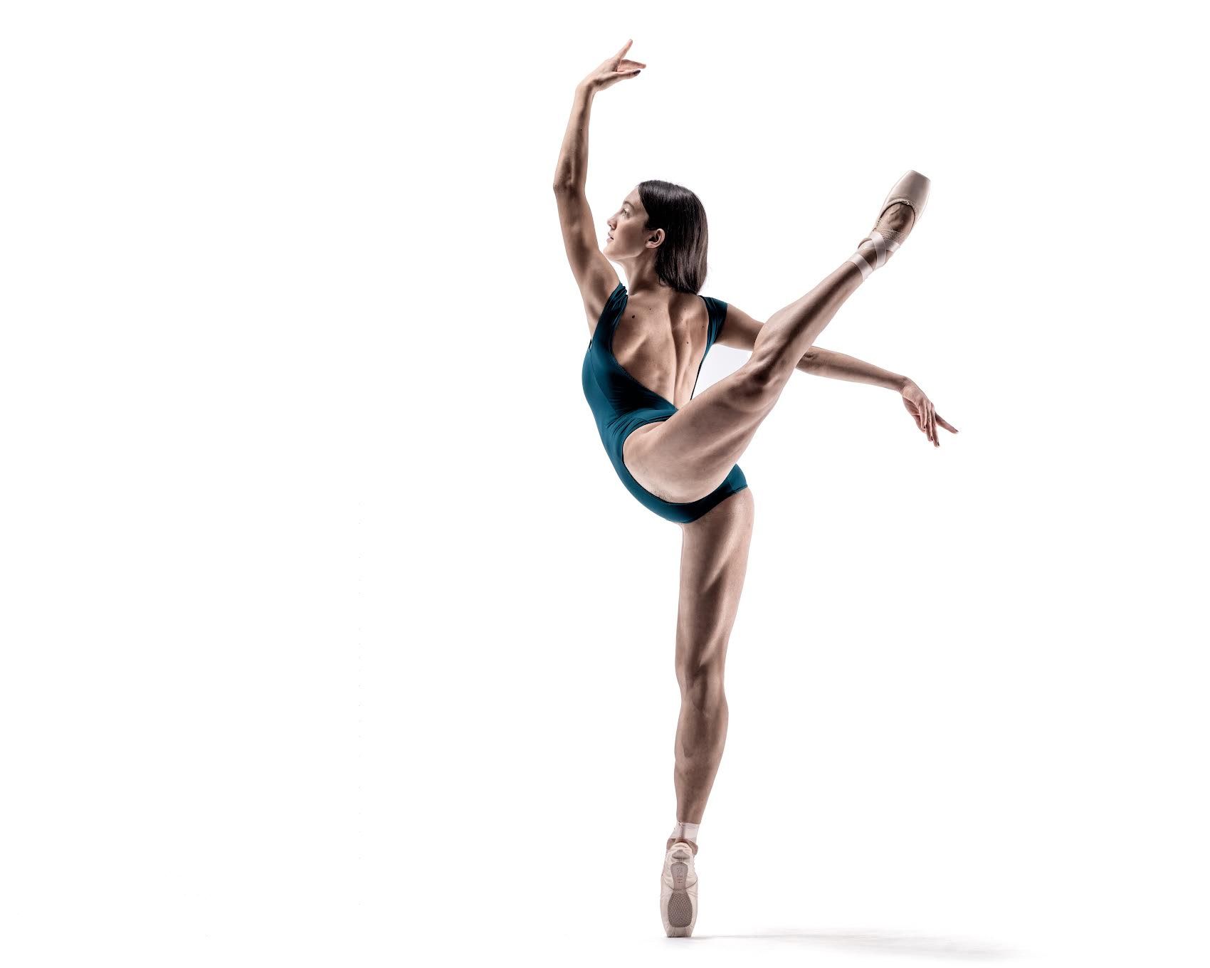 Ballerina in teal leotard, en pointe with leg extended, arm raised, against white backdrop.