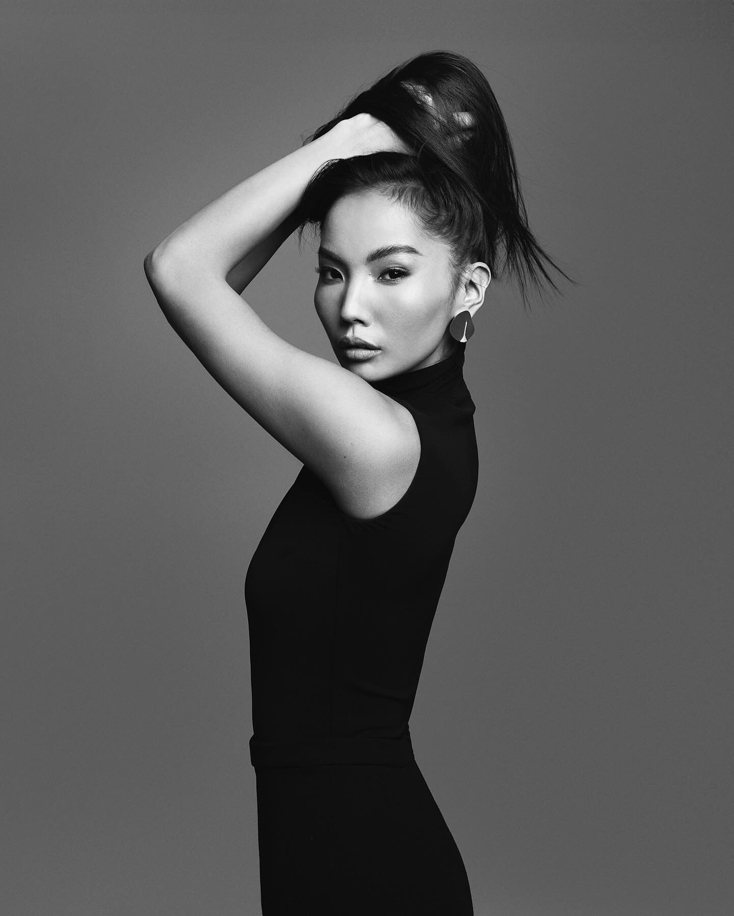 Woman in black turtleneck, pulling up hair into a high ponytail.