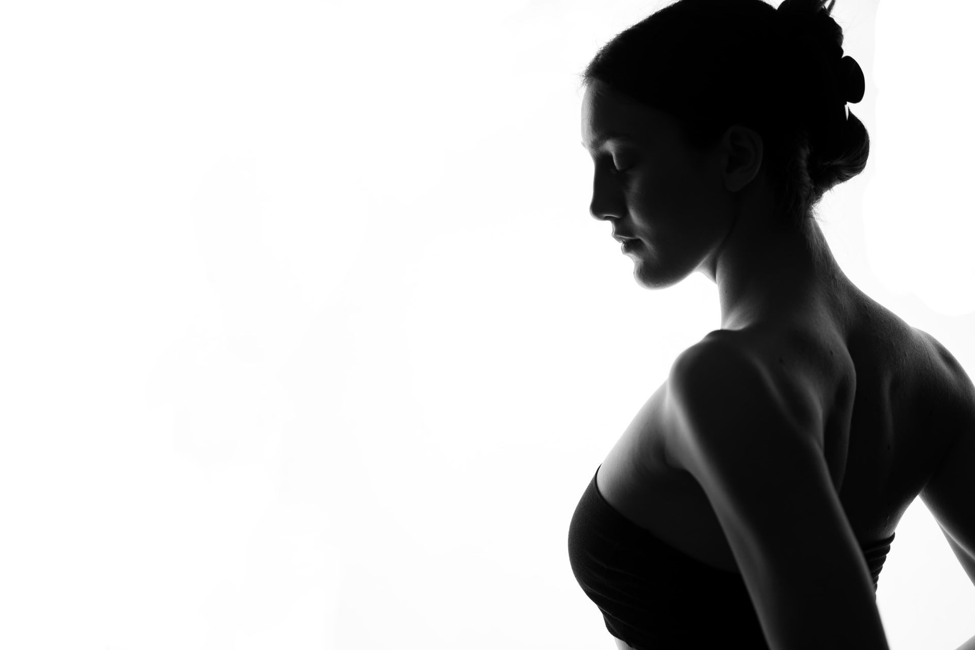 Silhouette of a person with hair up, looking down to the right; wearing a dark strapless top.