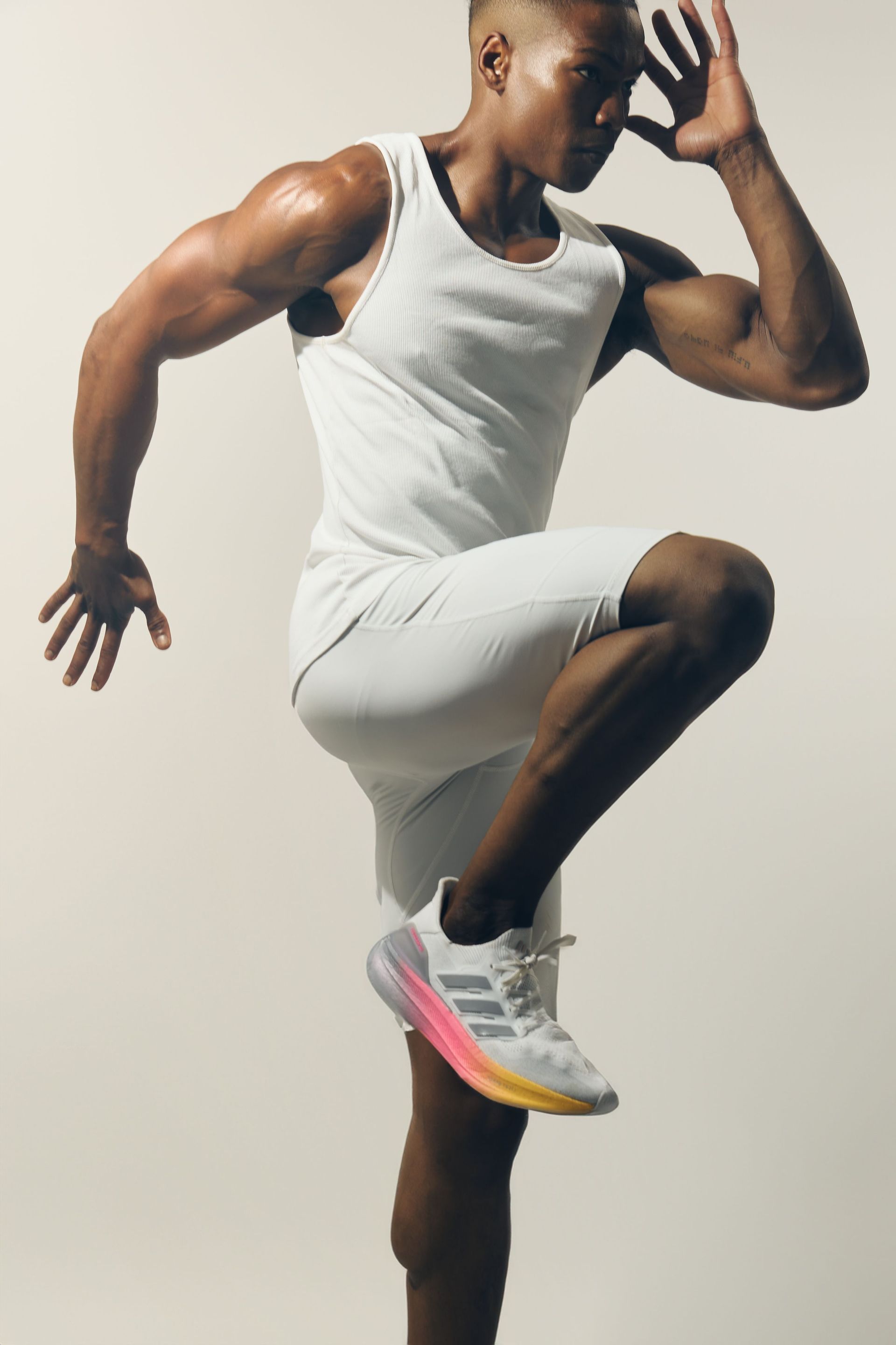 Man in white workout gear doing a high-knee exercise, athletic shoes, against a white background.