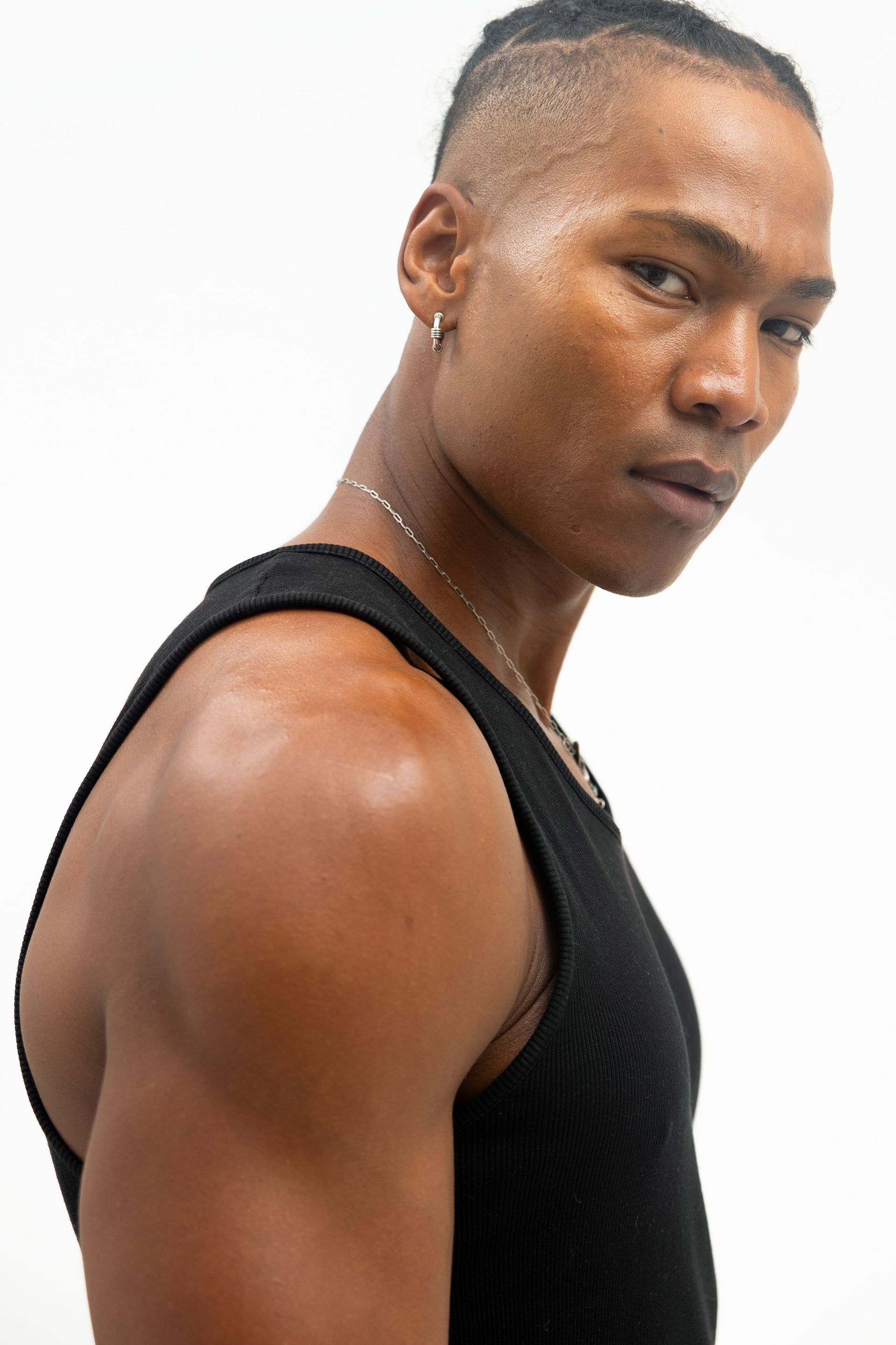 Man in black tank top, side view, looking at camera. Shoulder exposed, ear piercing visible, against white background.