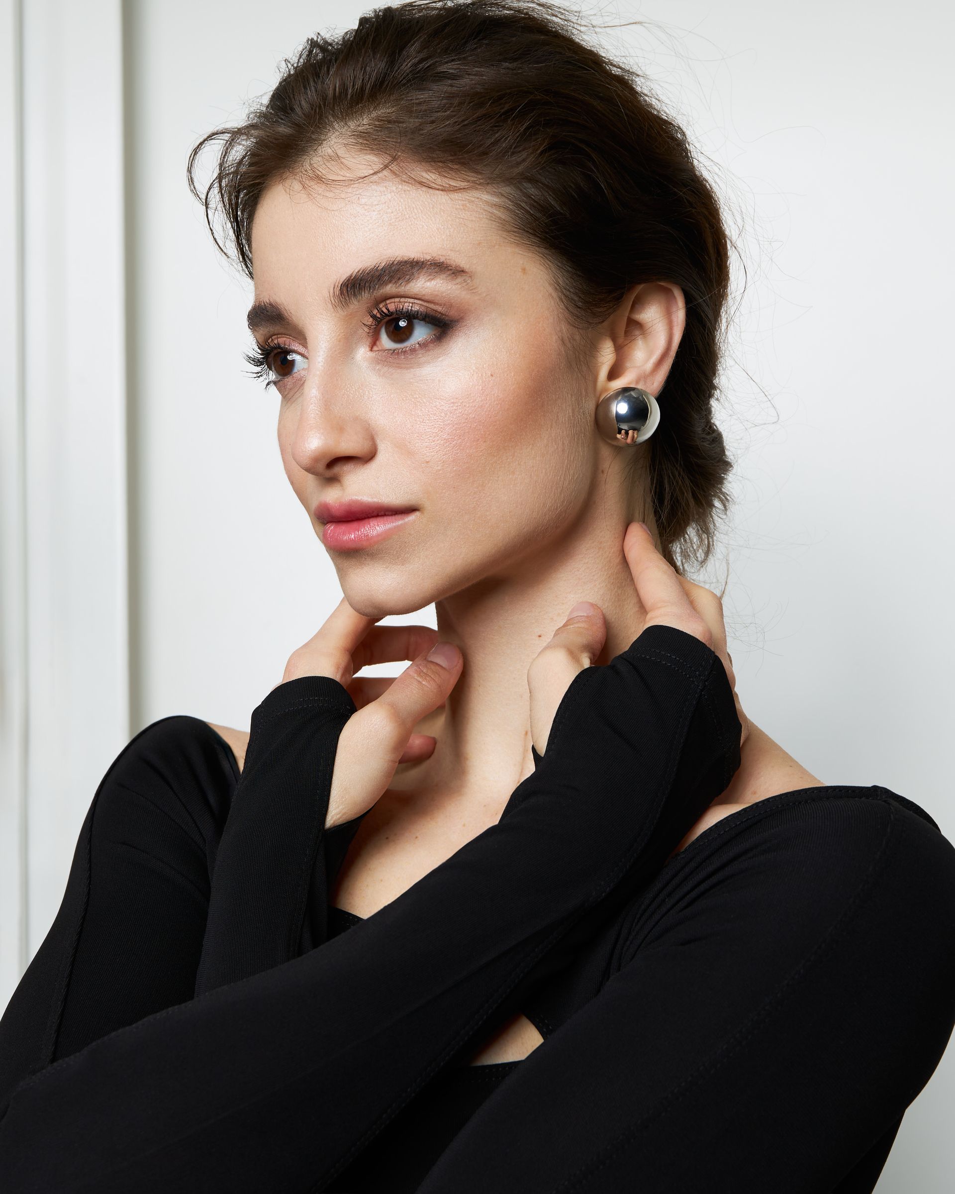 Woman with dark hair, wearing a black top and silver earrings, touching her neck.