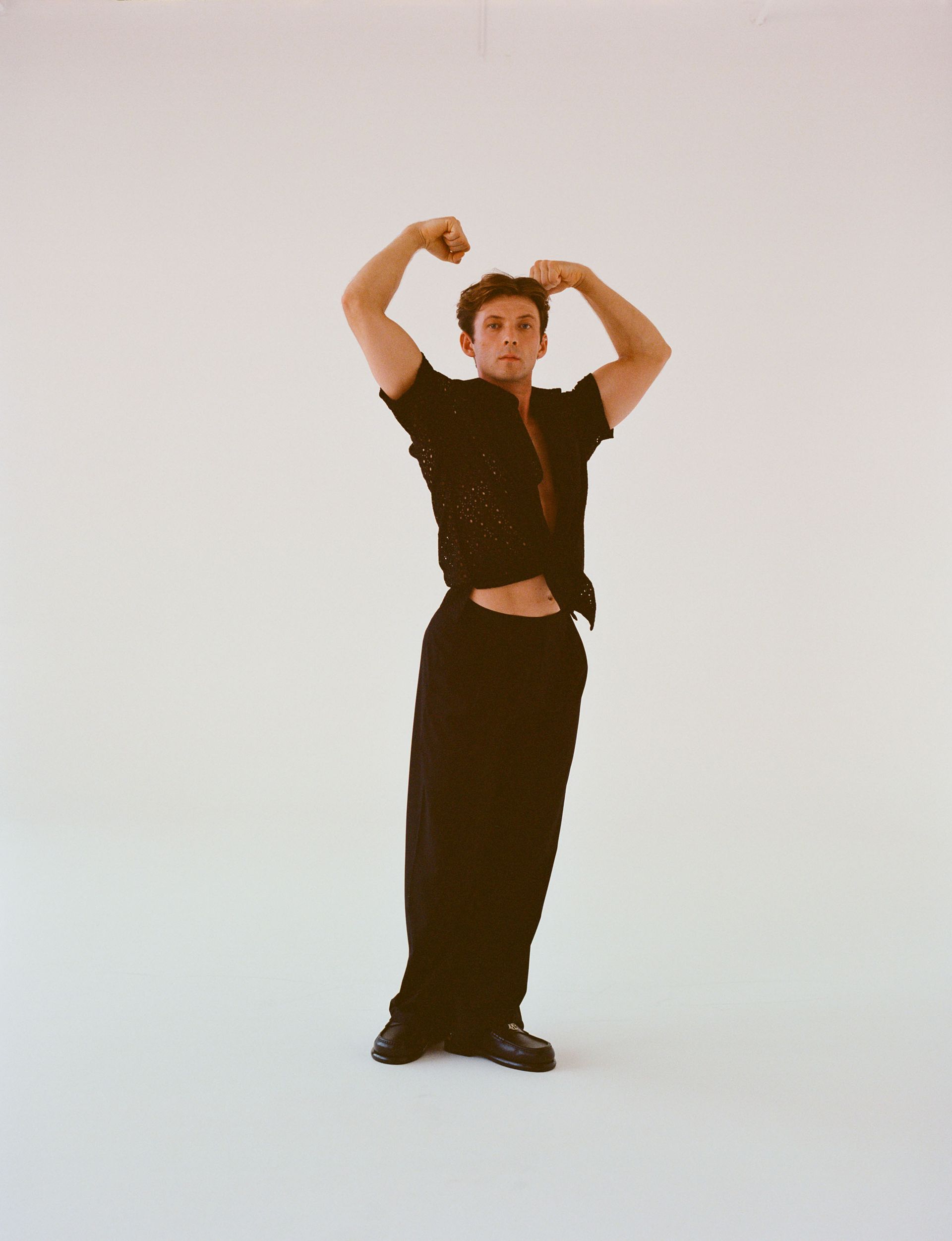 Man flexes in a black shirt and pants against a white background.
