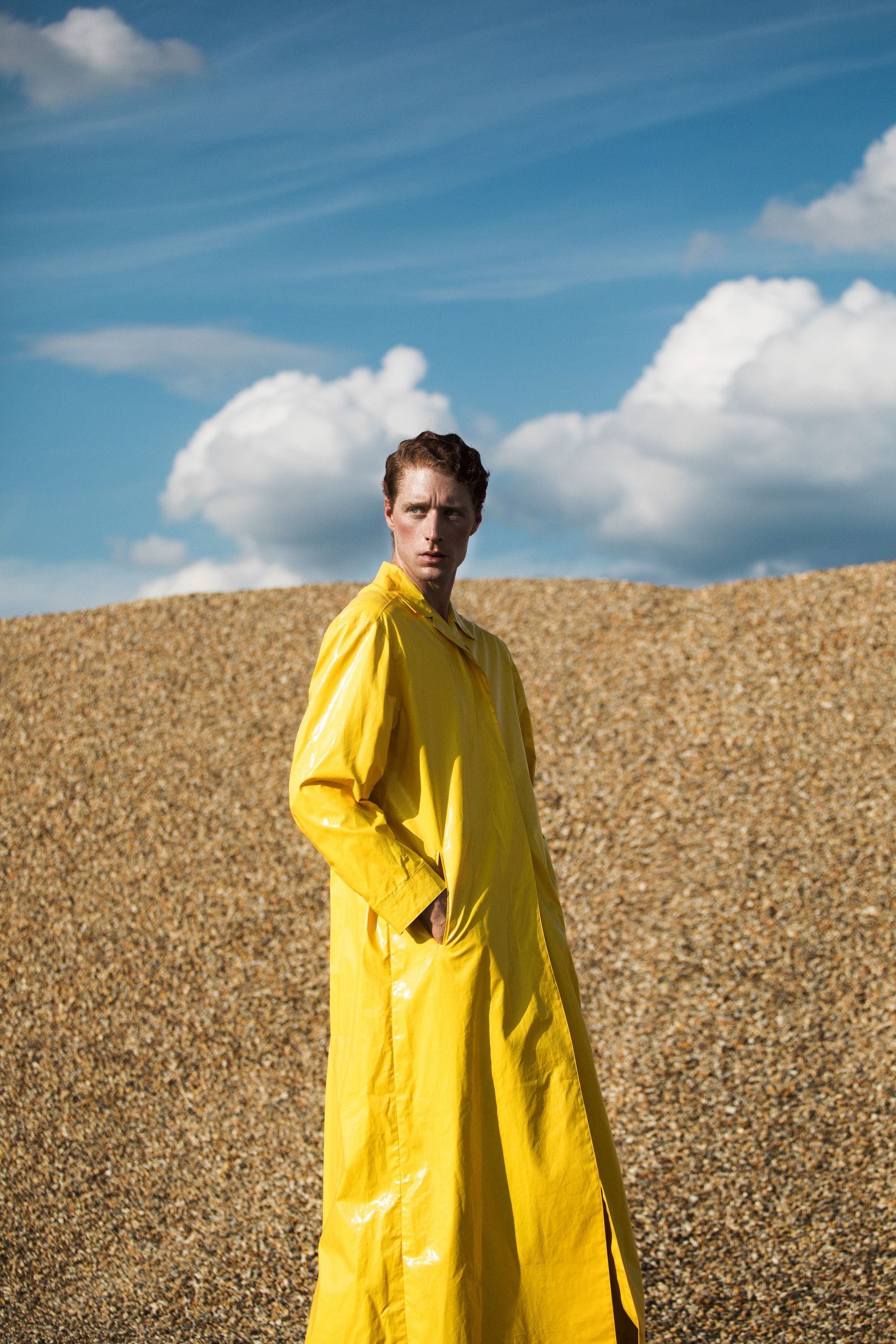 Man in a yellow raincoat standing in front of a pile of straw against a blue sky.