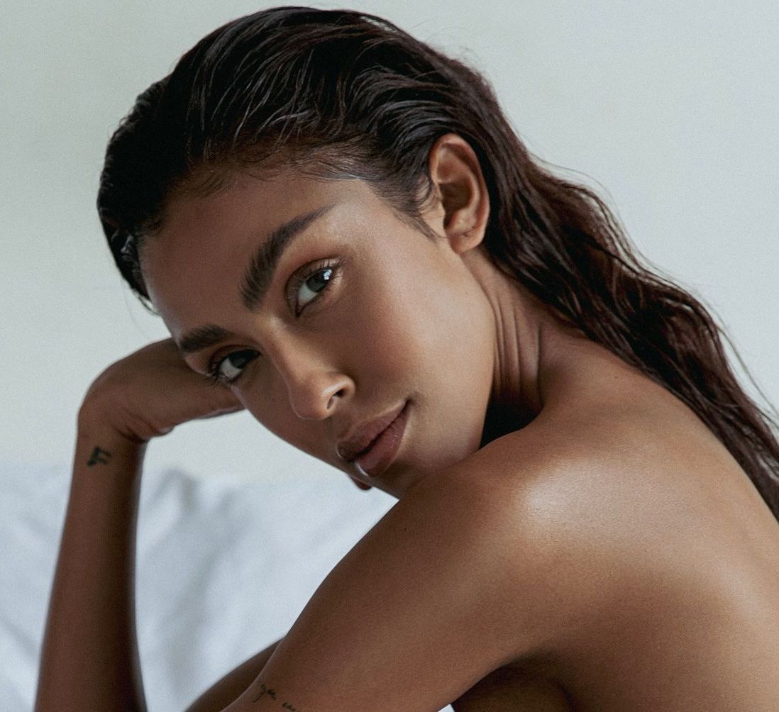 Woman with dark skin, wet hair, and a lip piercing, looking at the viewer.