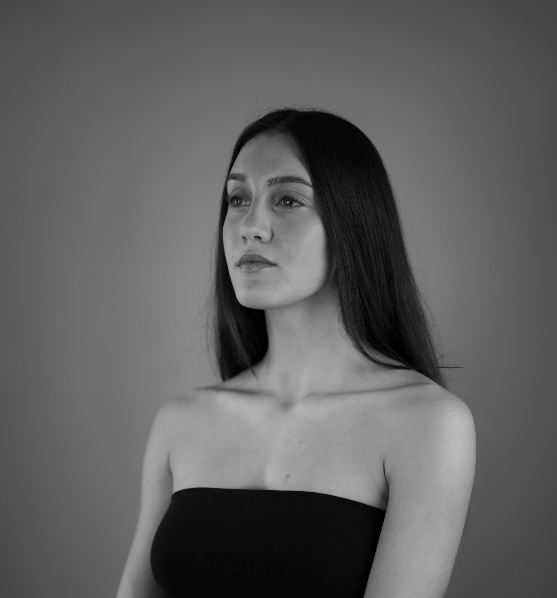 Woman in a strapless top looking away, black and white studio portrait.