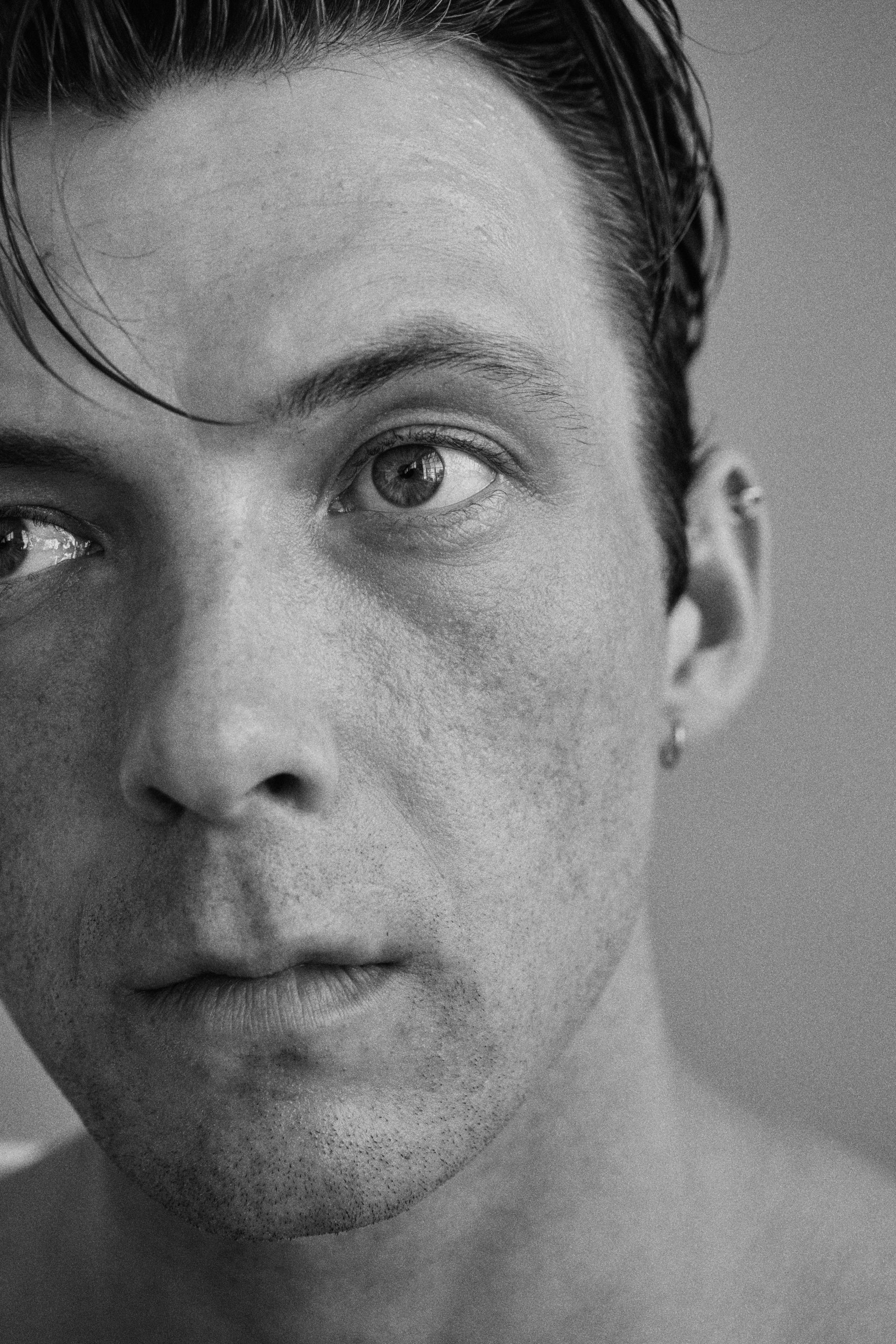 Man's close-up portrait. He looks slightly to the side with an intense expression. Black and white.