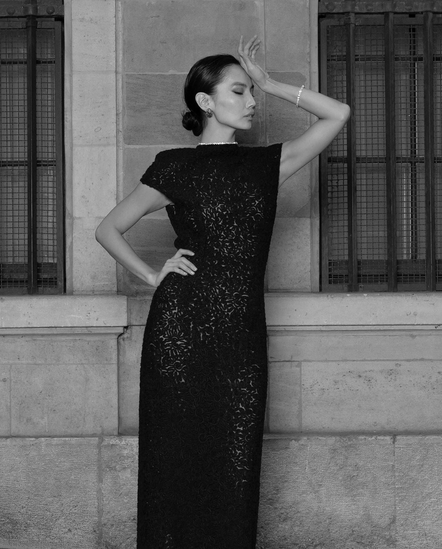 Woman in sequined dress poses against a stone wall, windows behind her.