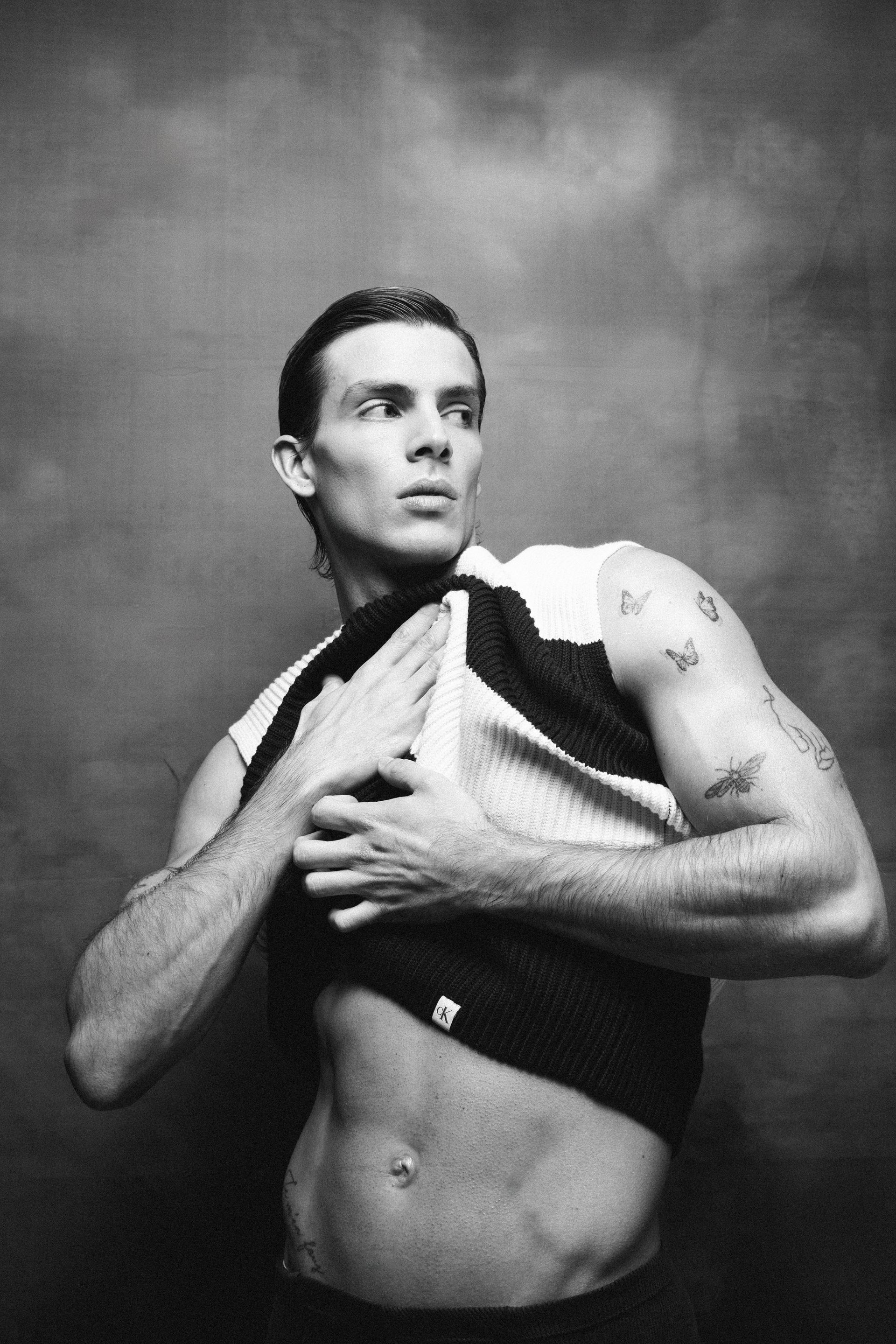Man pulling up his sleeveless shirt, revealing abdomen. Black and white photo.