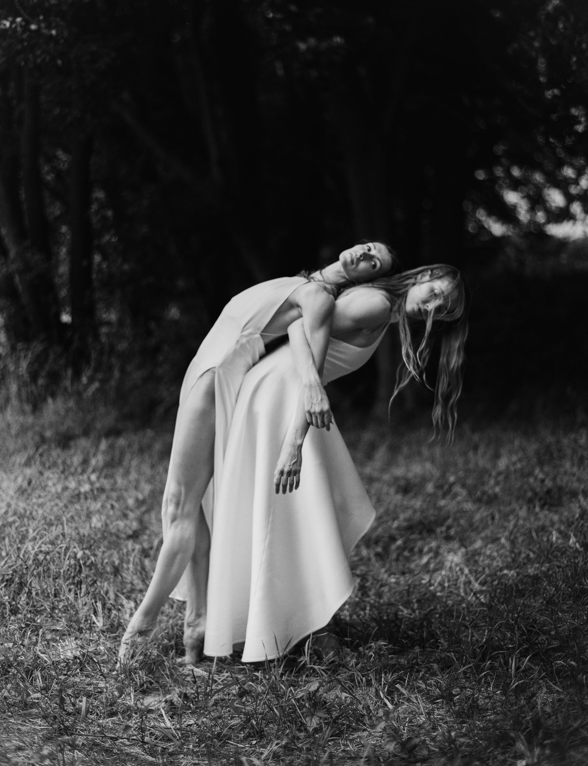 Two people, in flowing white dresses, dancing in a grassy field.