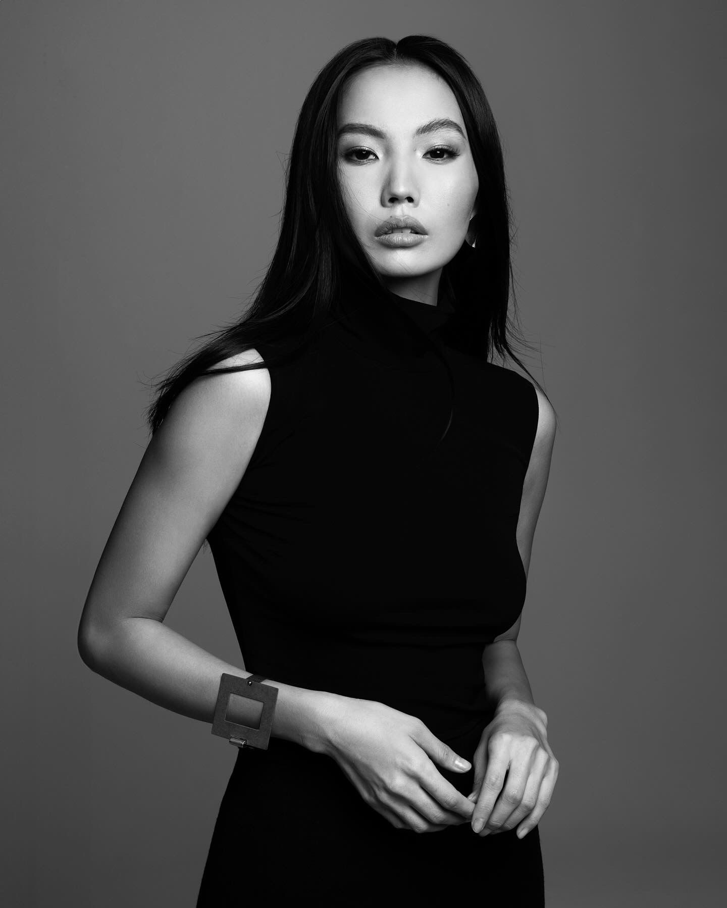 Woman in black sleeveless dress, looking to the side. Gray background.