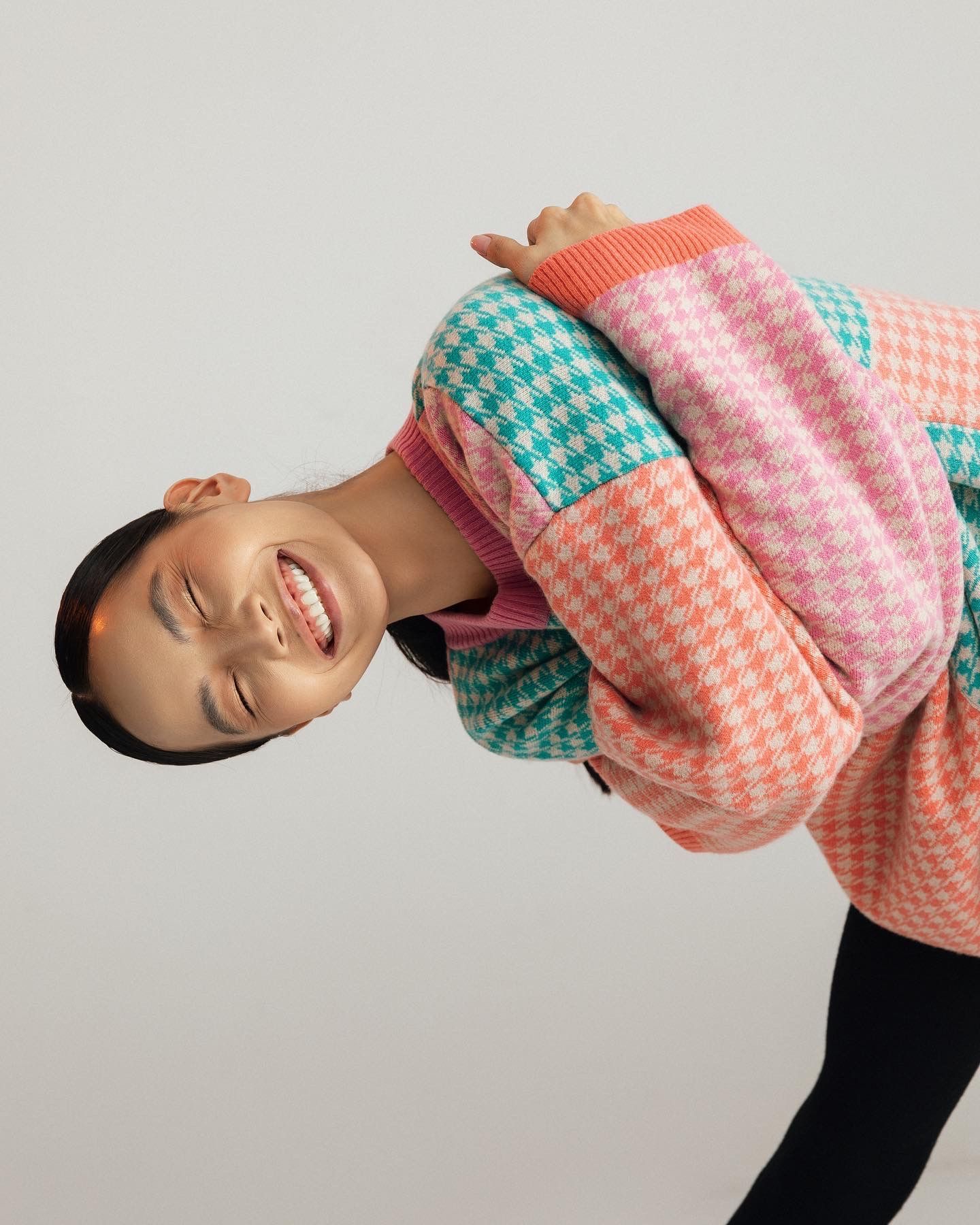 Person leaning, smiling, wearing a colorful houndstooth sweater.