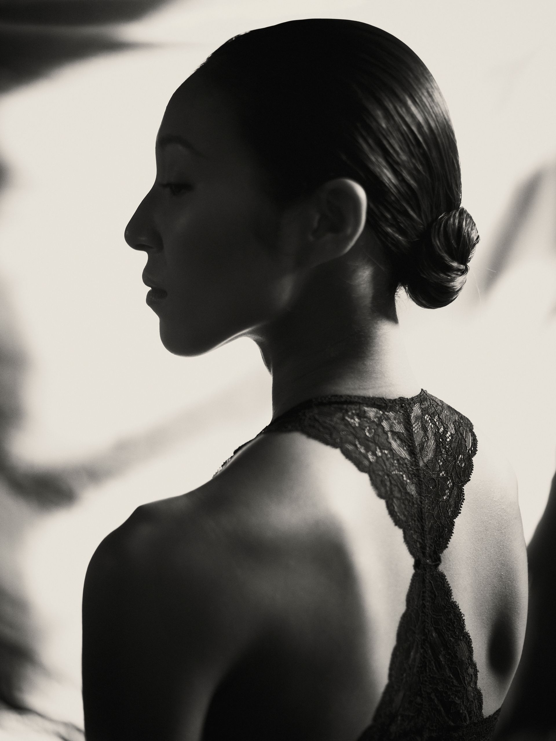 Woman in profile with hair pulled back, wearing a lacy top, lit in black and white.