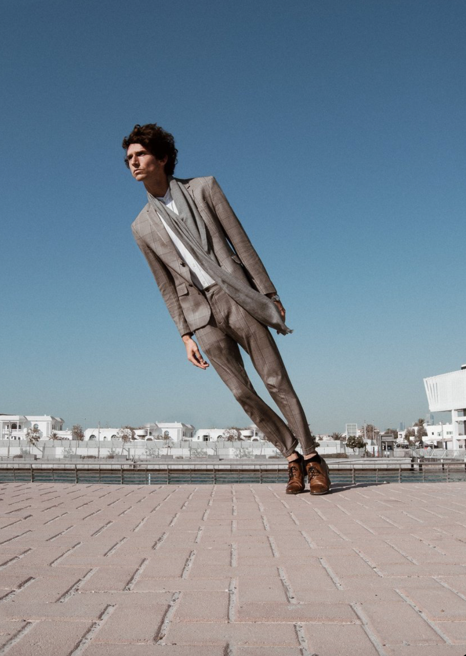 Man in gray suit leans, sky background.
