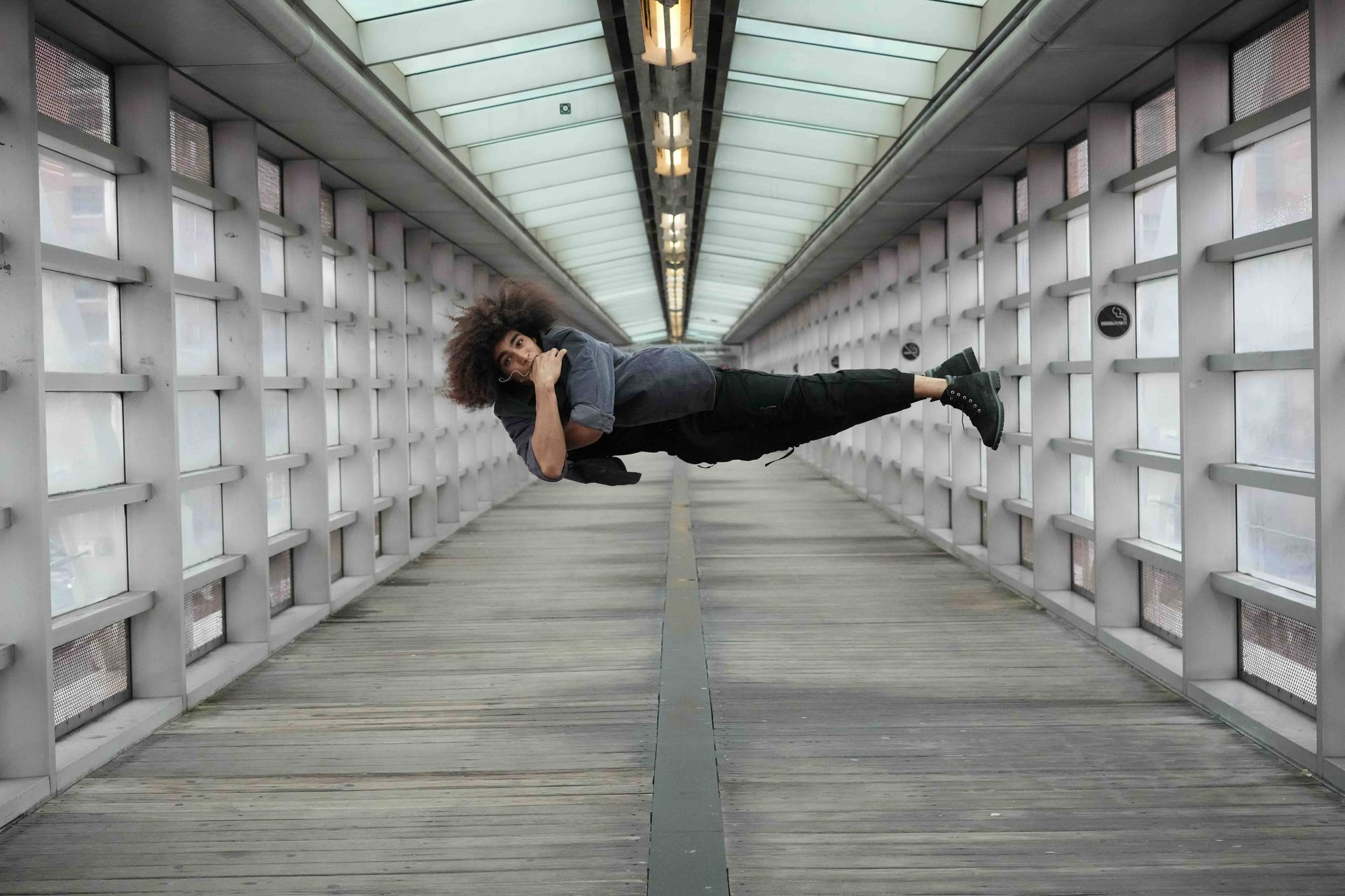 Person floating horizontally in a long, brightly lit hallway with glass windows.
