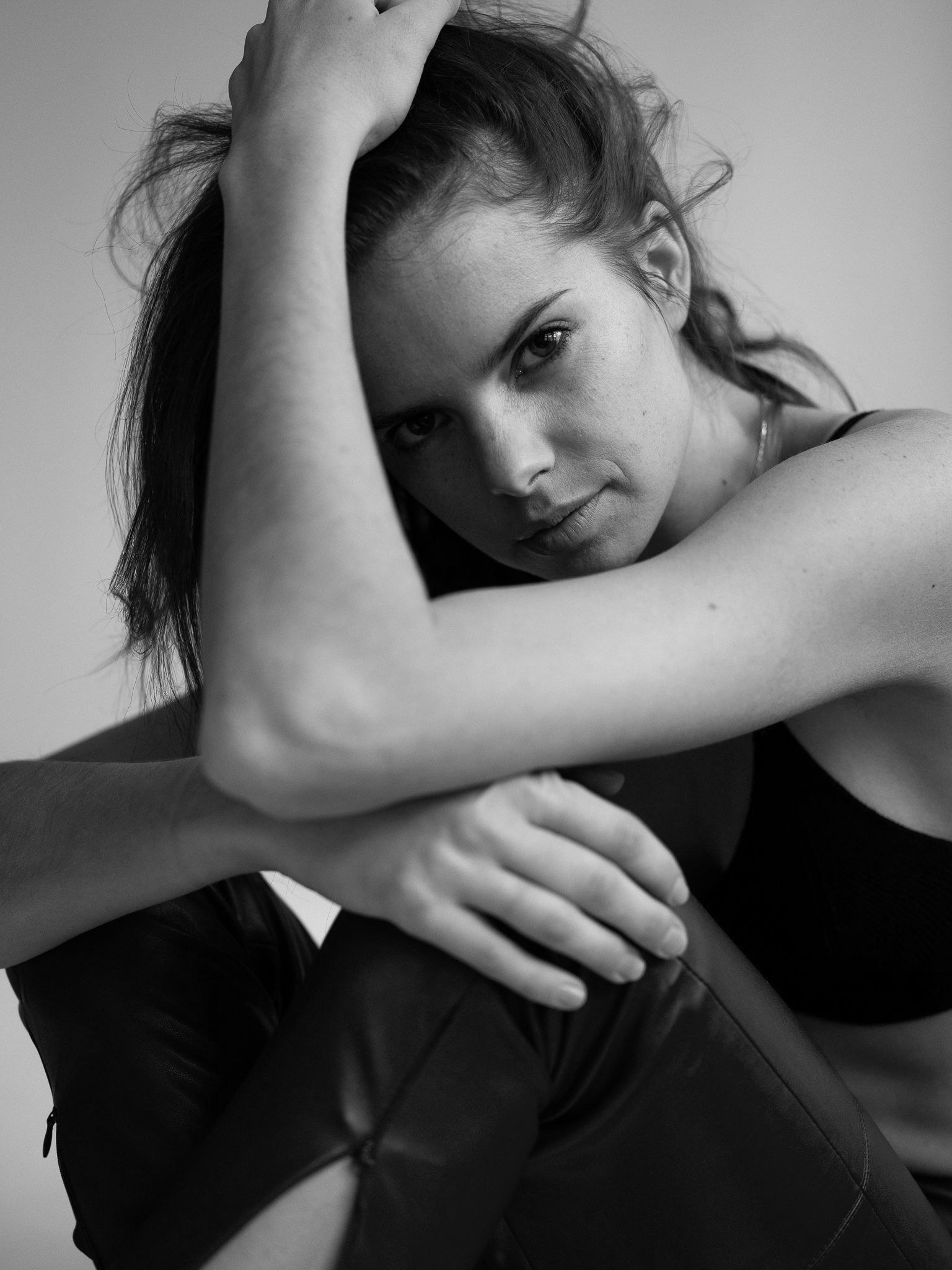Woman with dark hair, looking intently at the camera, arms crossed, seated.