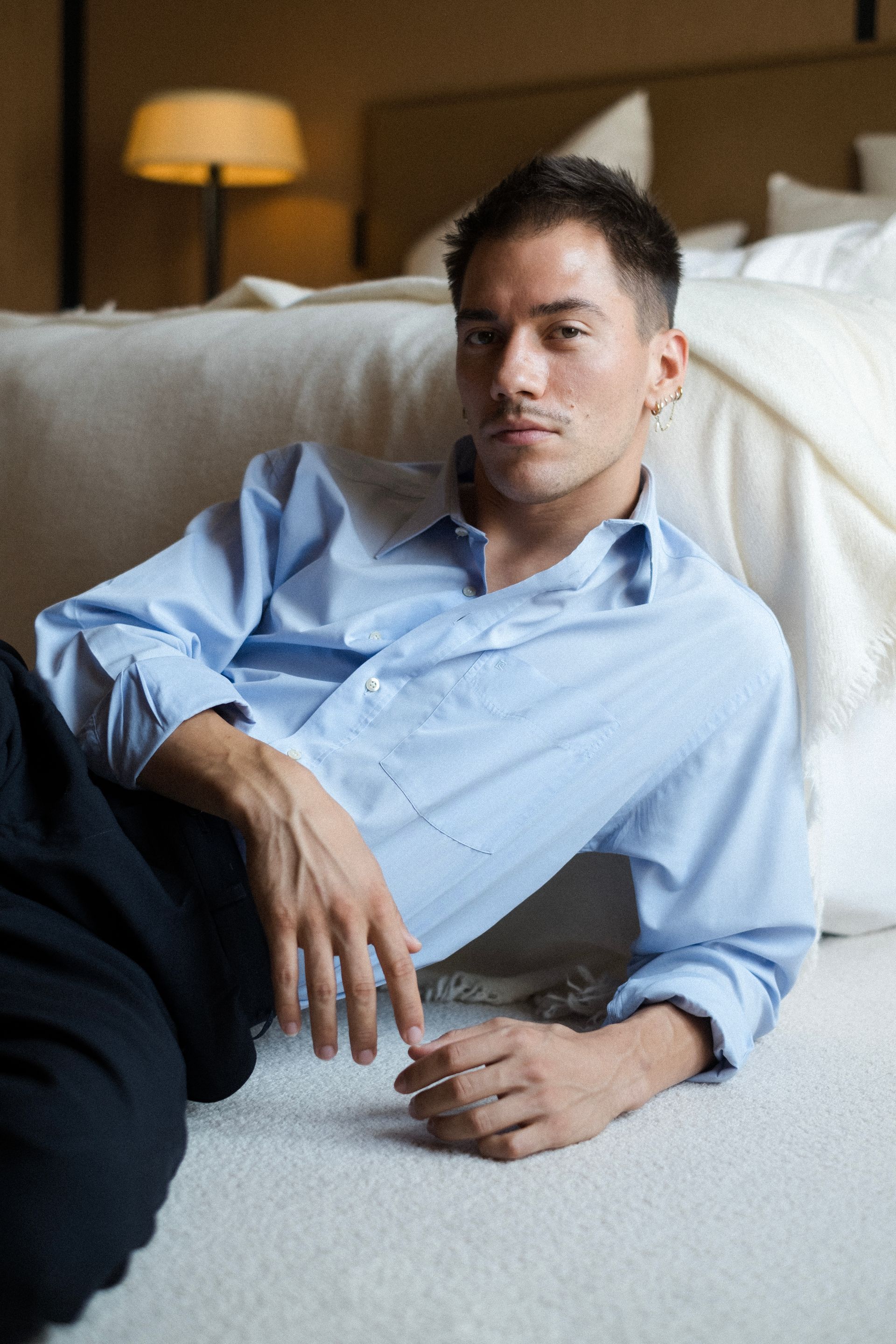 Man in light blue shirt and dark pants reclines on a carpet next to a bed.