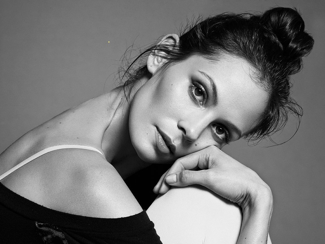 Woman with dark hair in a bun, resting head on arm, looking thoughtful, black and white photo.