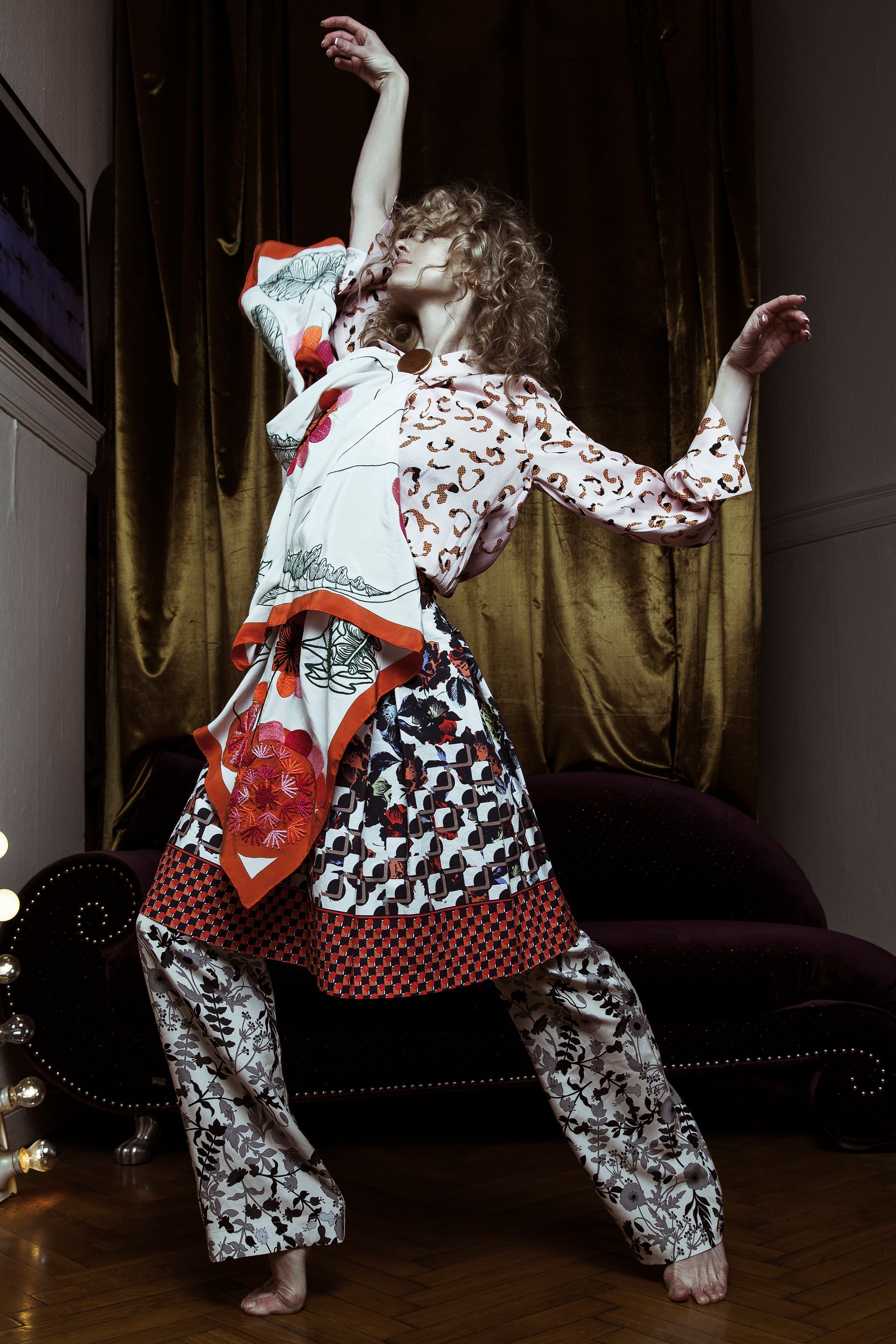 Woman in patterned outfit dances with arms raised in dimly lit room.