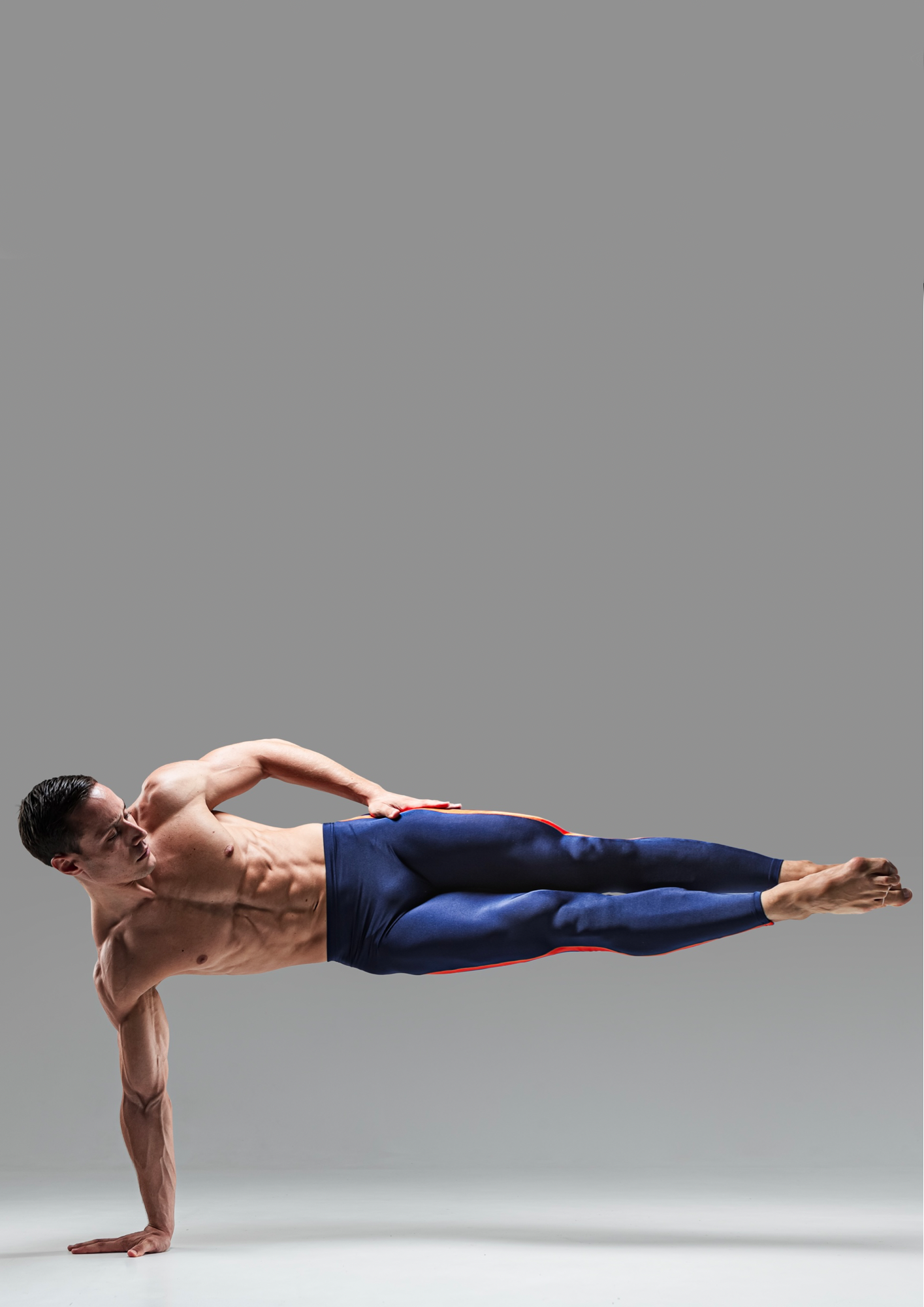 Man in a side plank pose on one arm, wearing dark leggings, against a gray background.