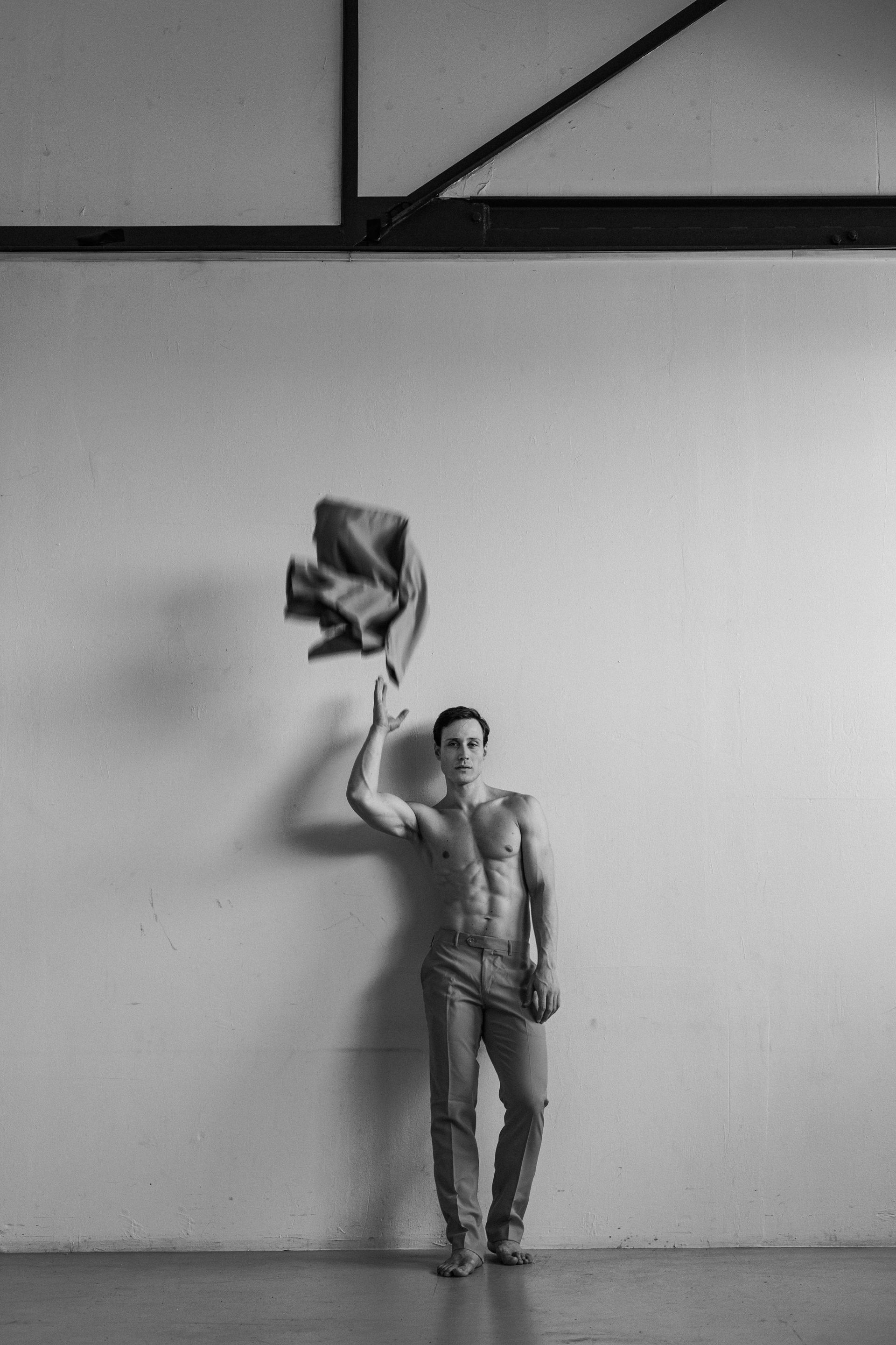 Shirtless person throws jacket in air next to a white wall.