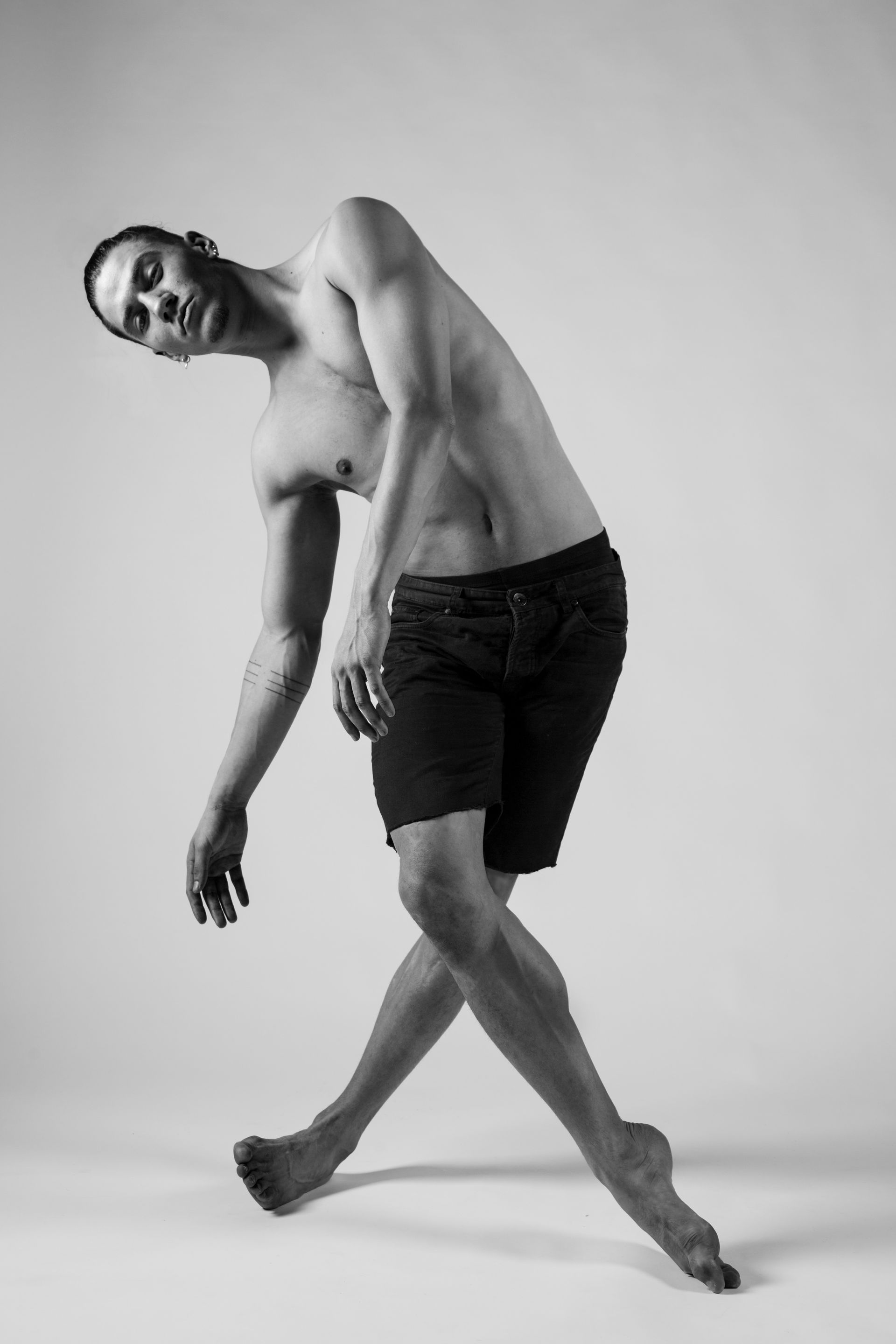 Male dancer in a dynamic pose, leaning to the left with crossed legs, in black and white.