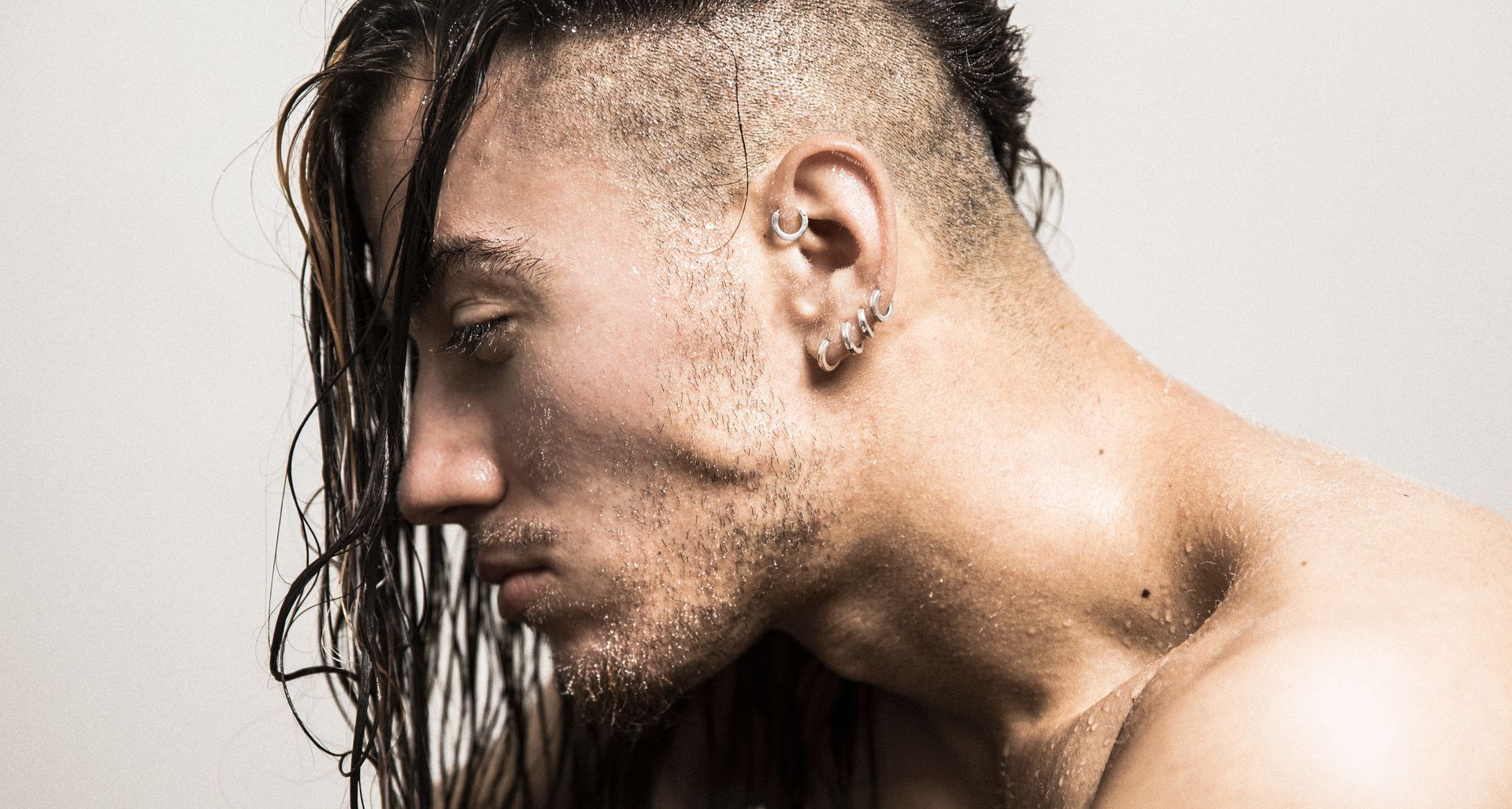Man with long wet hair, shaved sides, droplets on skin, looking down, side profile.