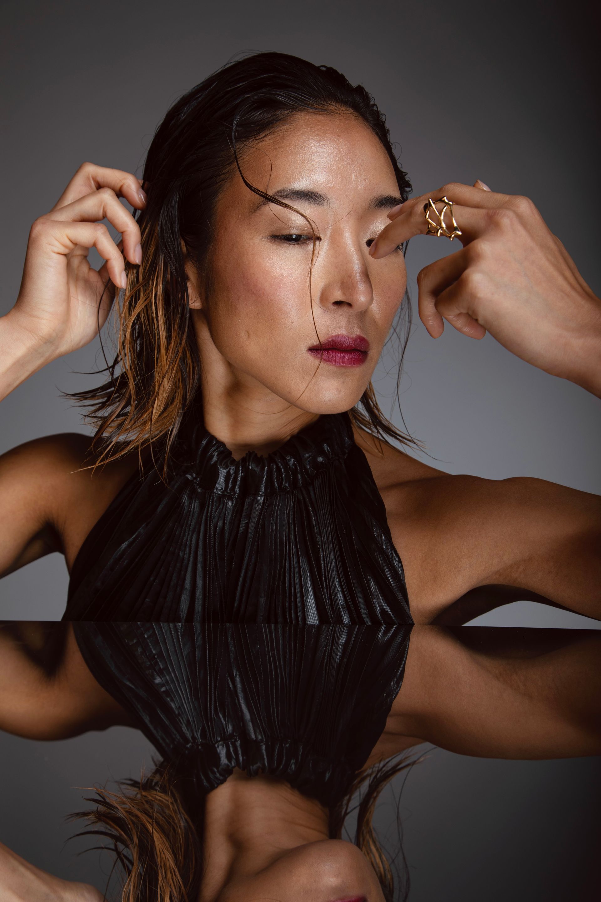 Woman in black halter top, touching her eye, with reflection.