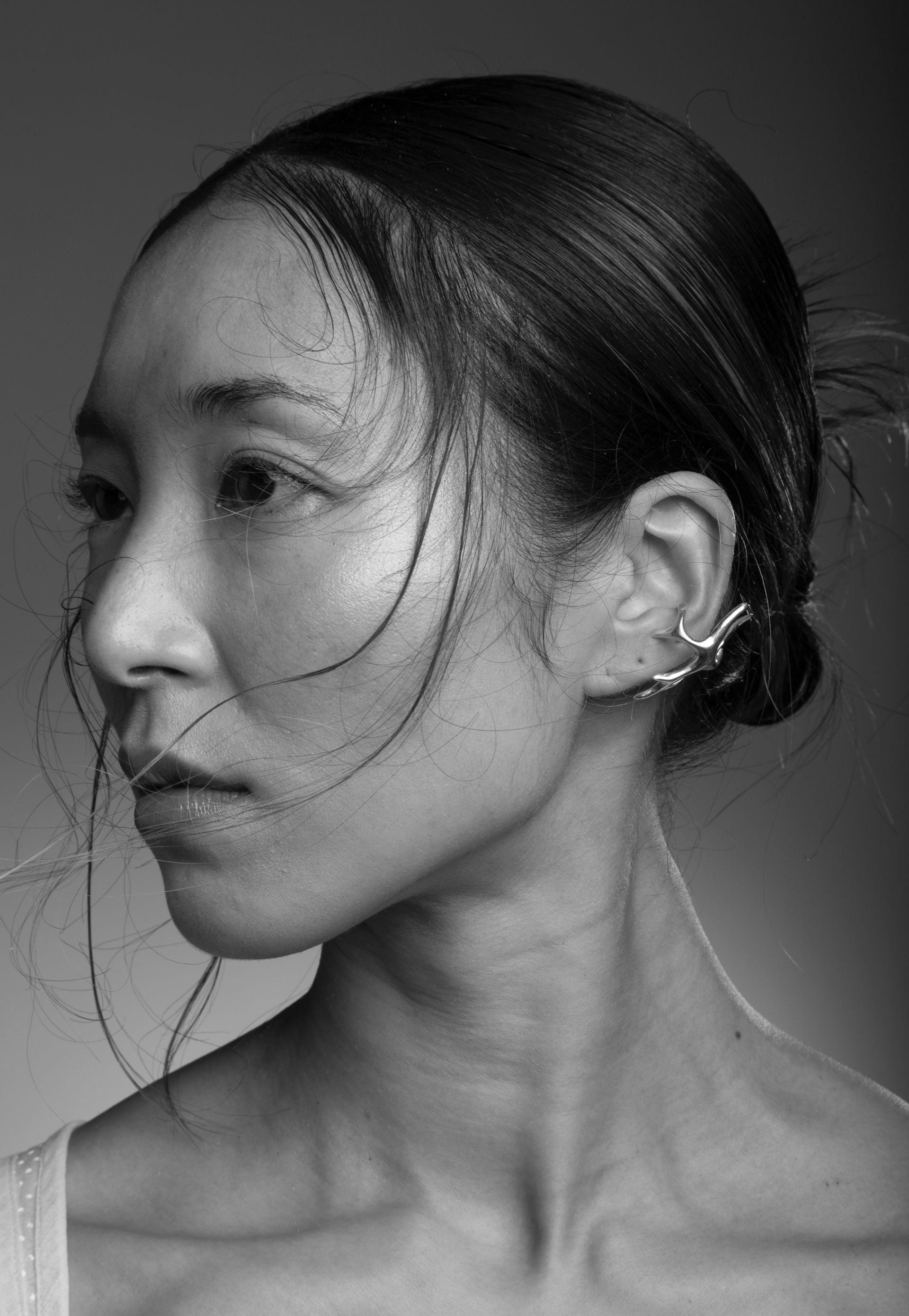 Woman with dark hair in a bun, wearing ear cuff, looking left, grayscale portrait.