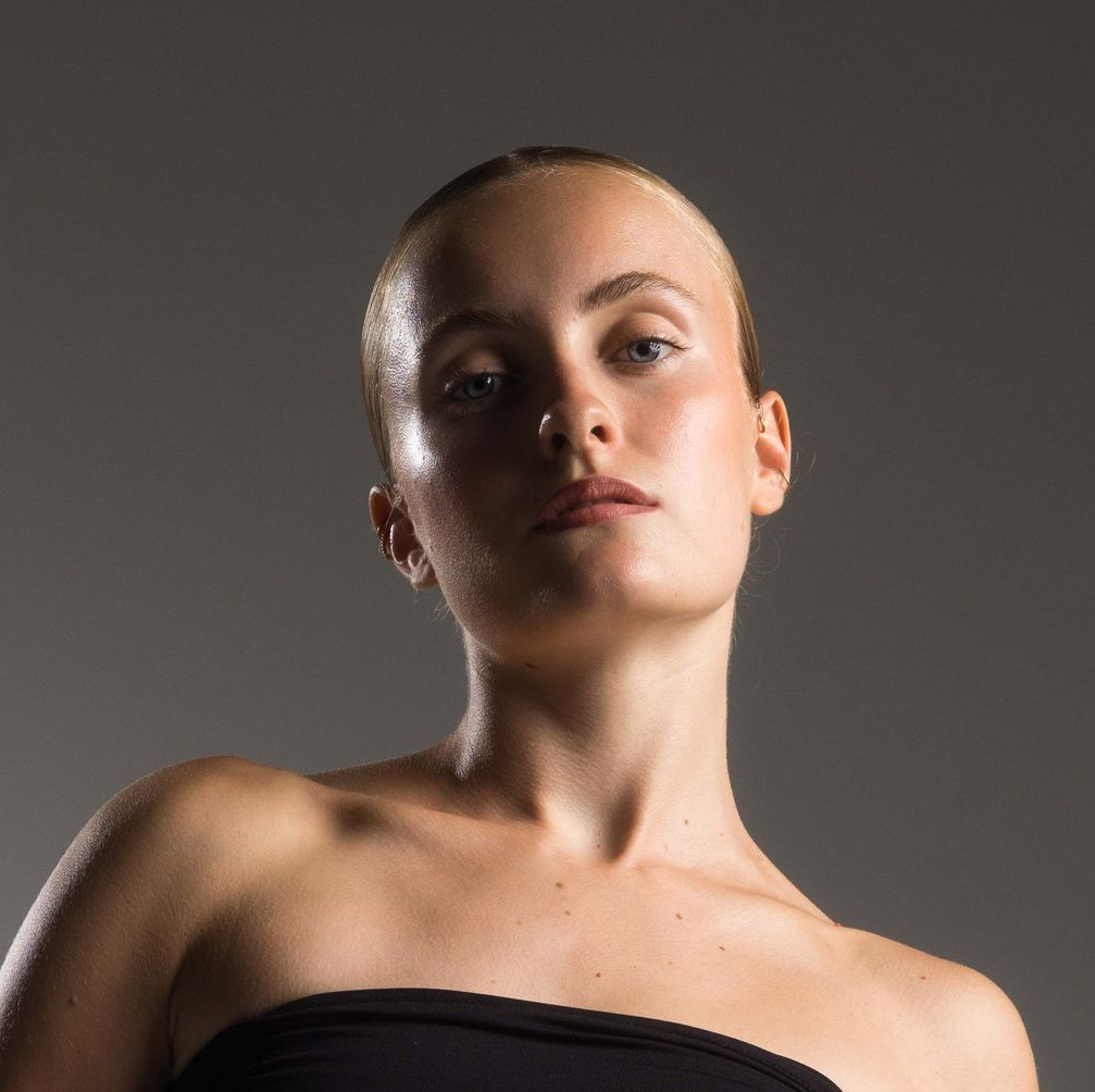 Woman in black strapless top, looking upward with a slight frown, lit from above, against a gray background.