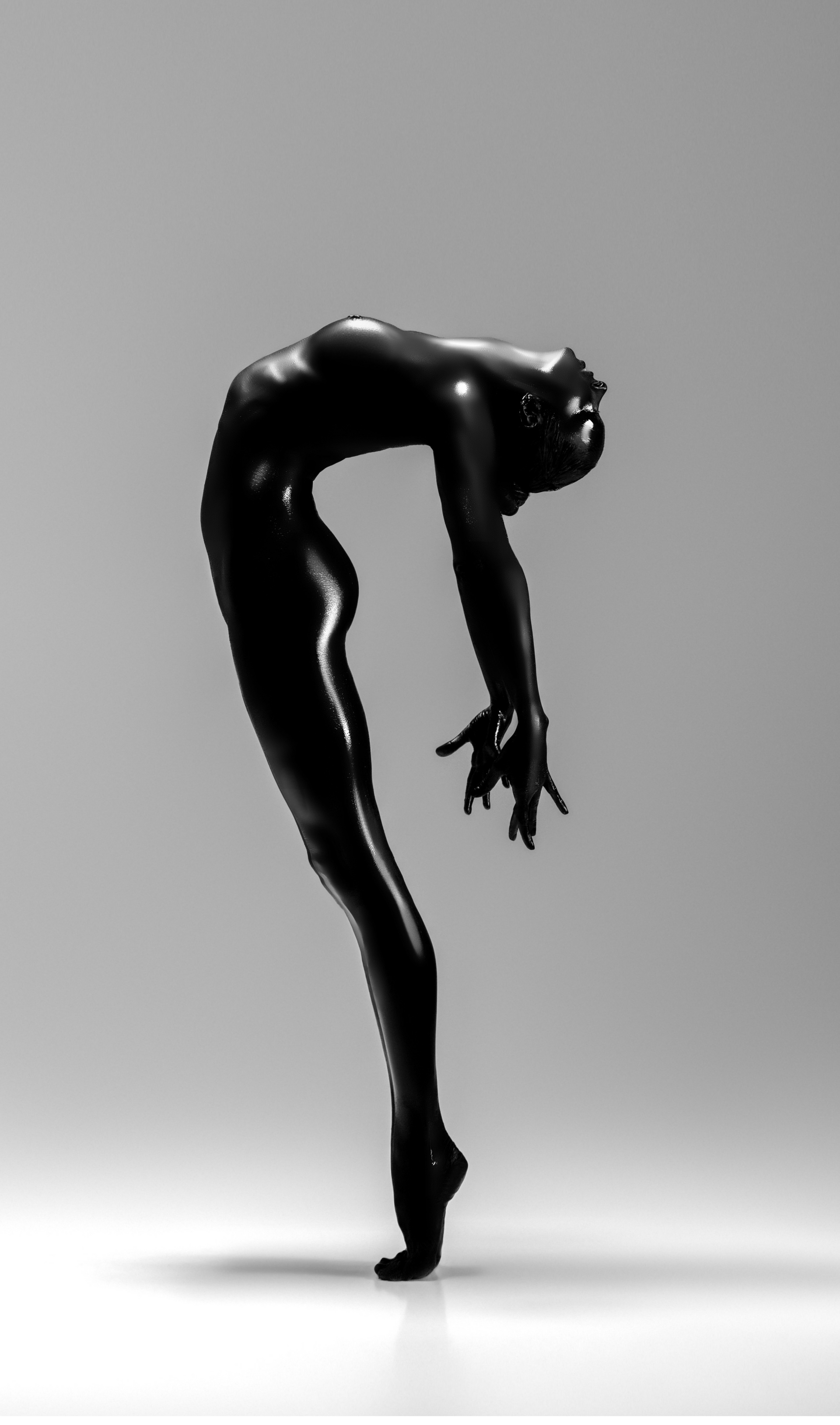 Ballet dancer in a curved pose, body painted black, against a white background.