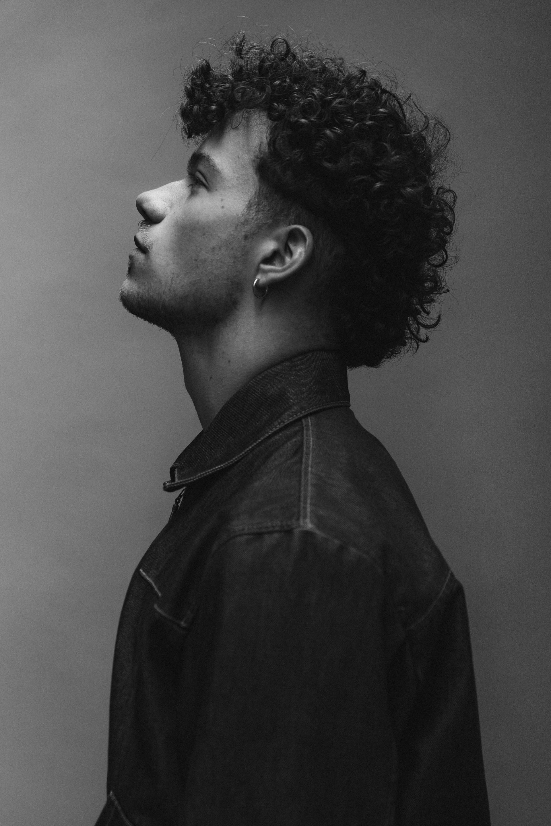 Man with curly hair, looking upward. Wearing a dark jacket. Black and white.