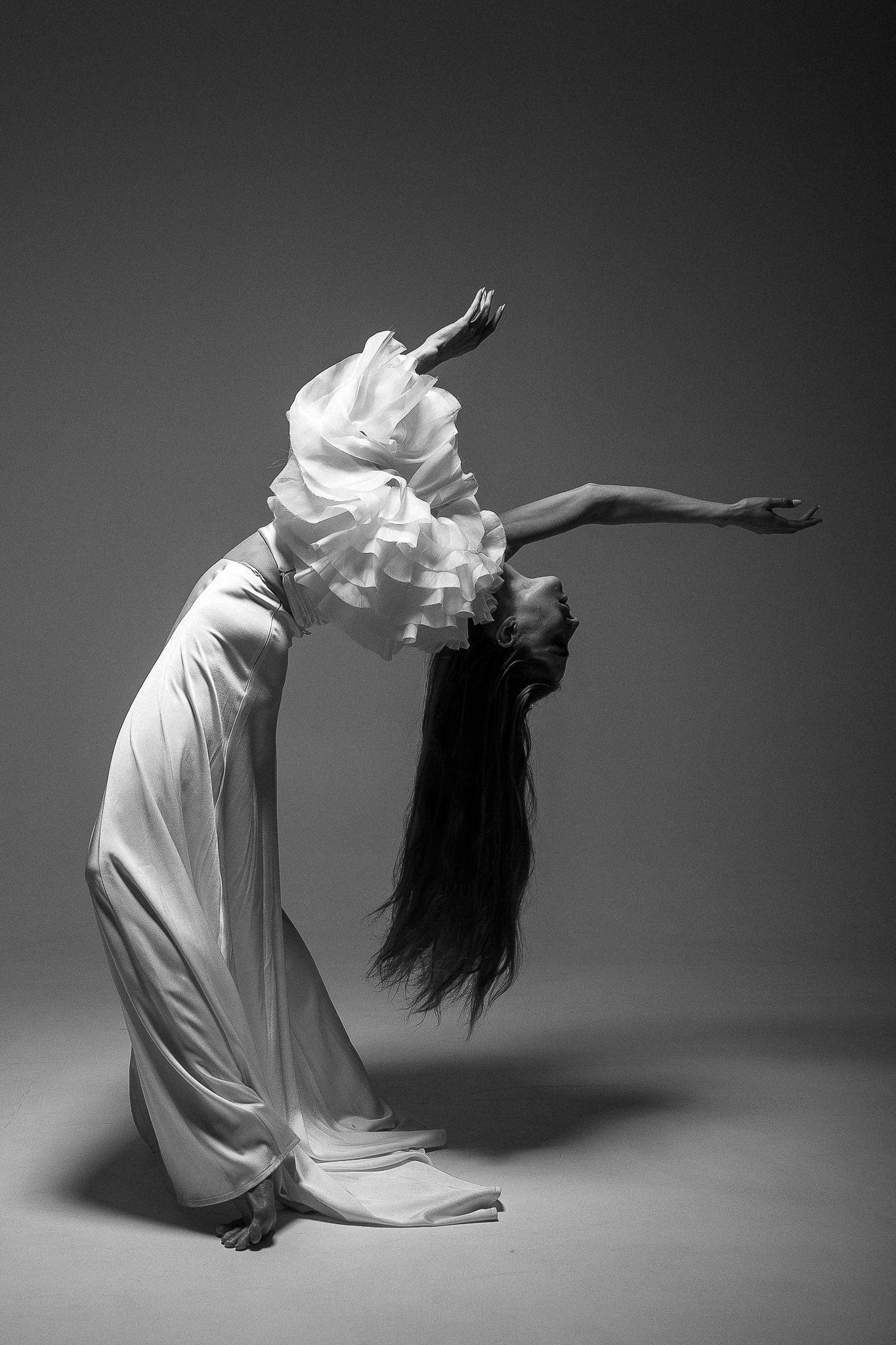 Woman in white dress arches back dramatically, arms outstretched. Black and white photo.