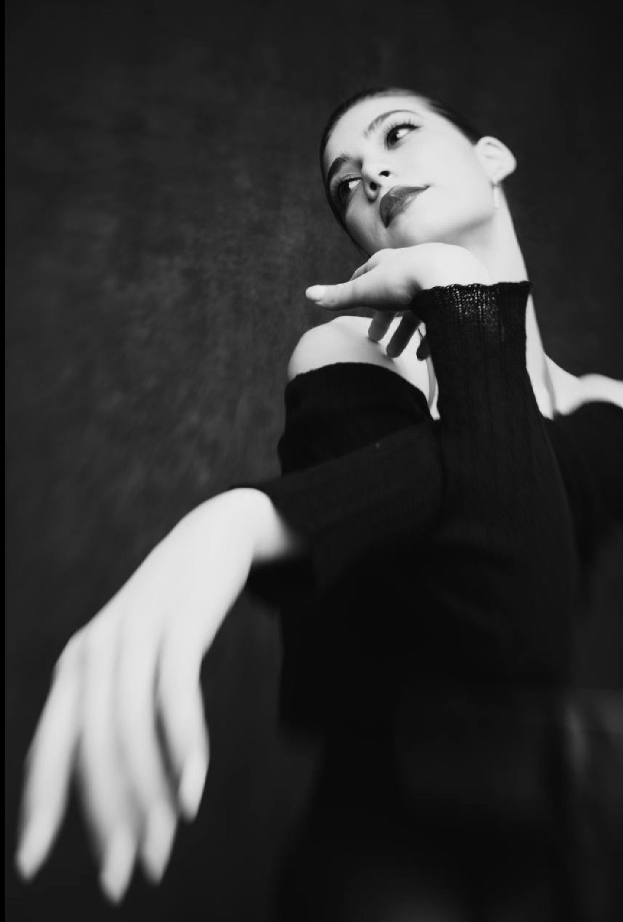 Ballerina in black, arms gracefully posed, dark background.