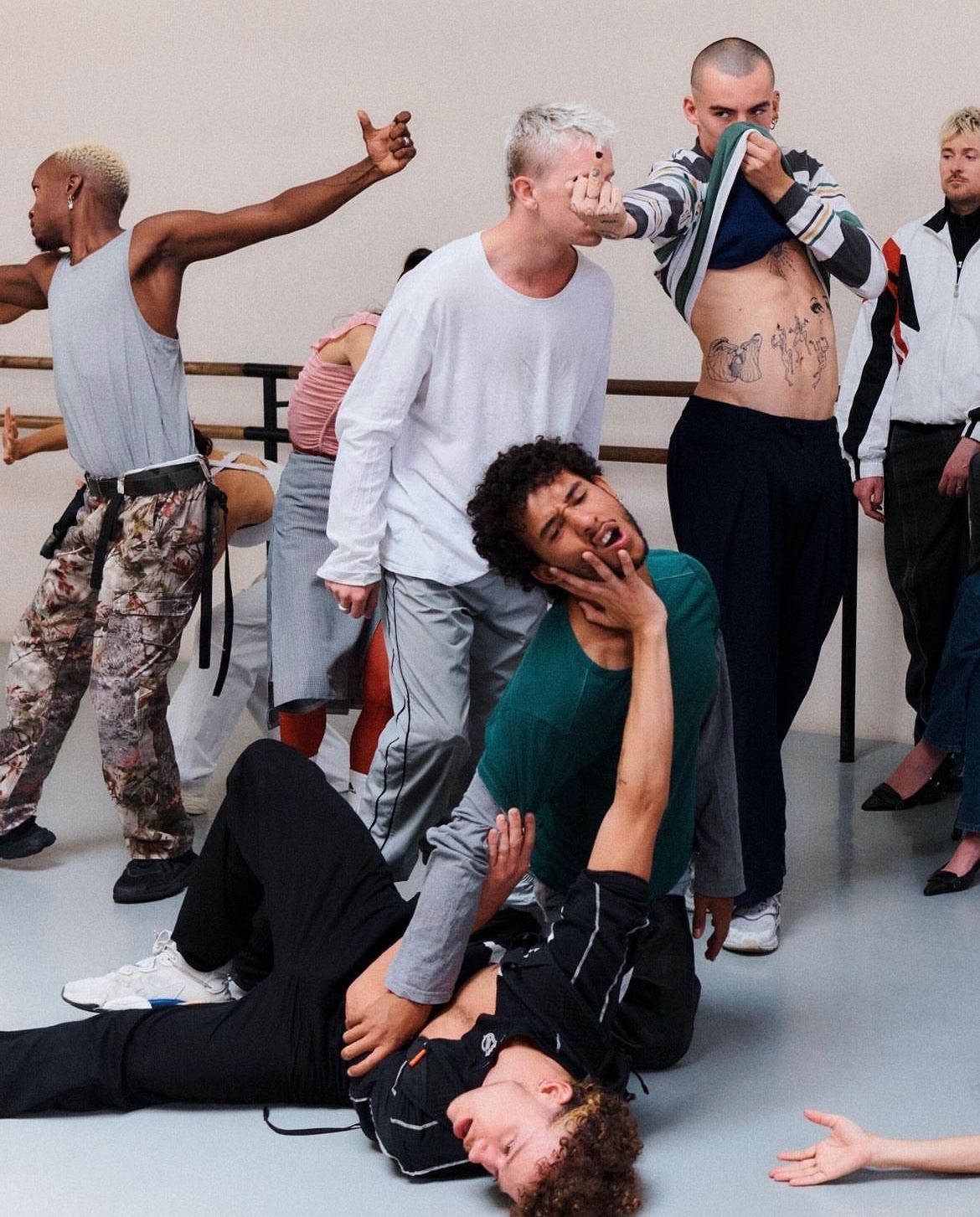 Dancers in a studio. Some are mid-movement, others appear engaged in a fight, emotions range from anger to fear.