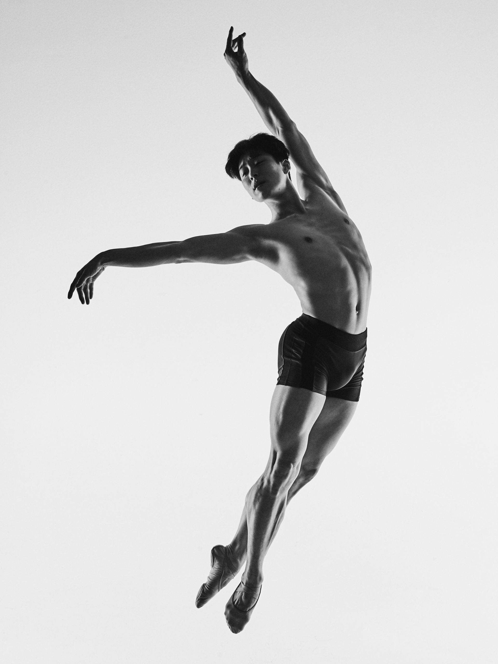 Ballet dancer leaping and gesturing with arms outstretched against a bright sky.