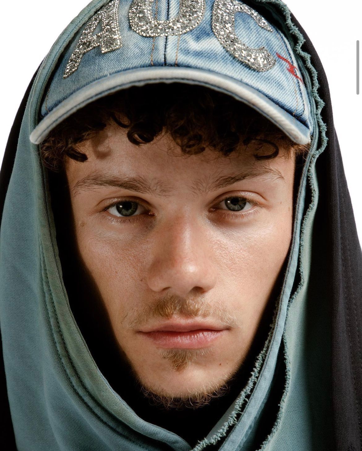 Man wearing a denim cap and hooded jacket, with “AOC” embellished on the cap.