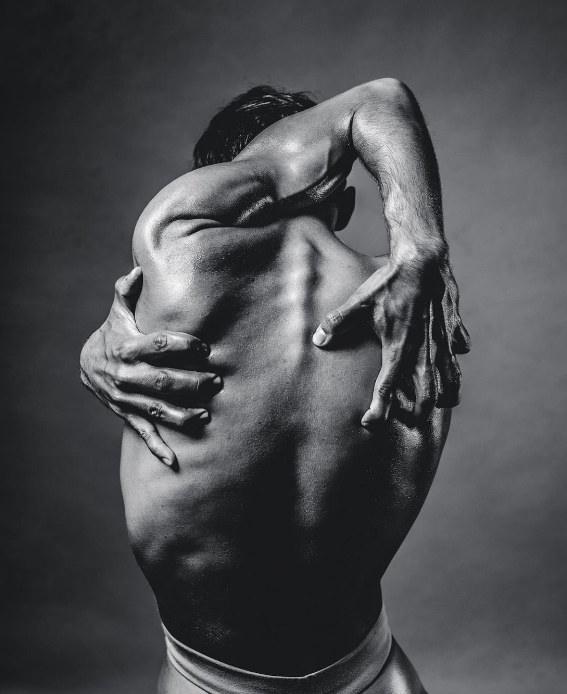 Person with back arched, arms wrapped around back, dark background.