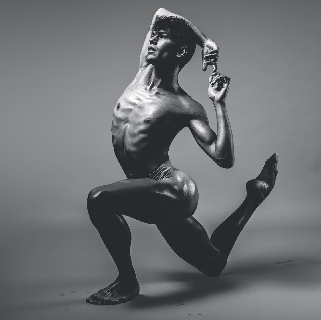Dancer in a dynamic pose. Leaning back with one leg extended and arm raised, in a studio with grey backdrop.