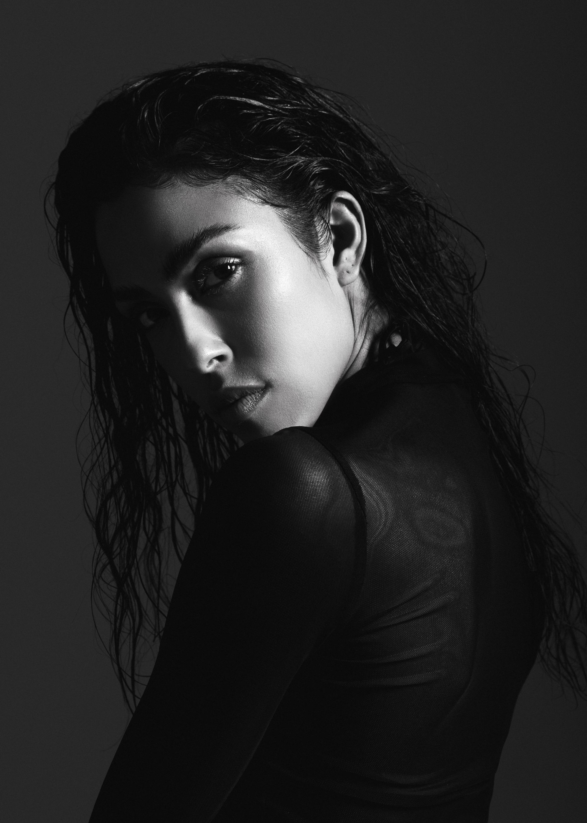 Woman with wet hair looking over her shoulder, wearing a textured dark top. Black and white.