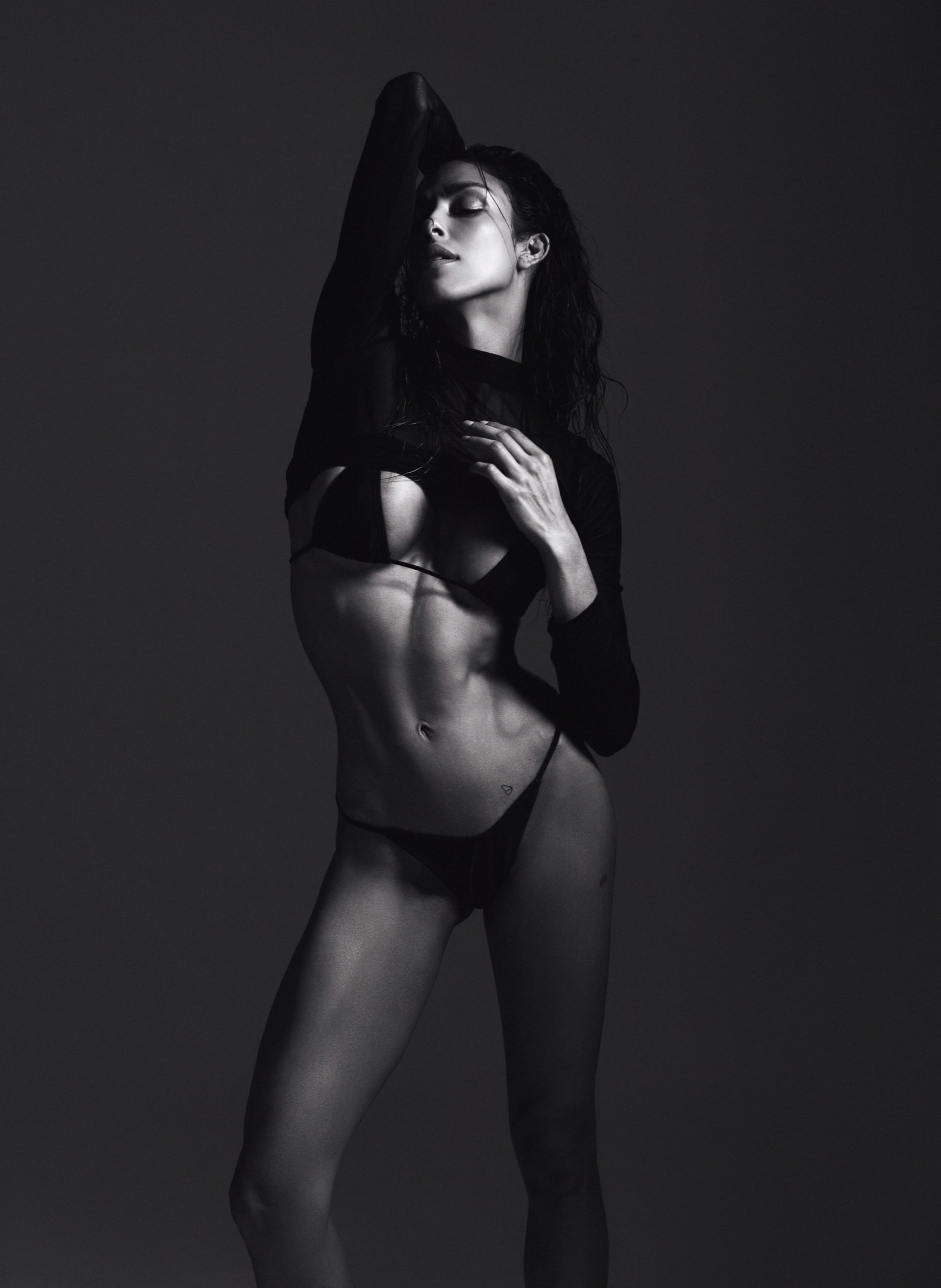 Woman in lingerie raising arm, toned abs, black and white studio shot.