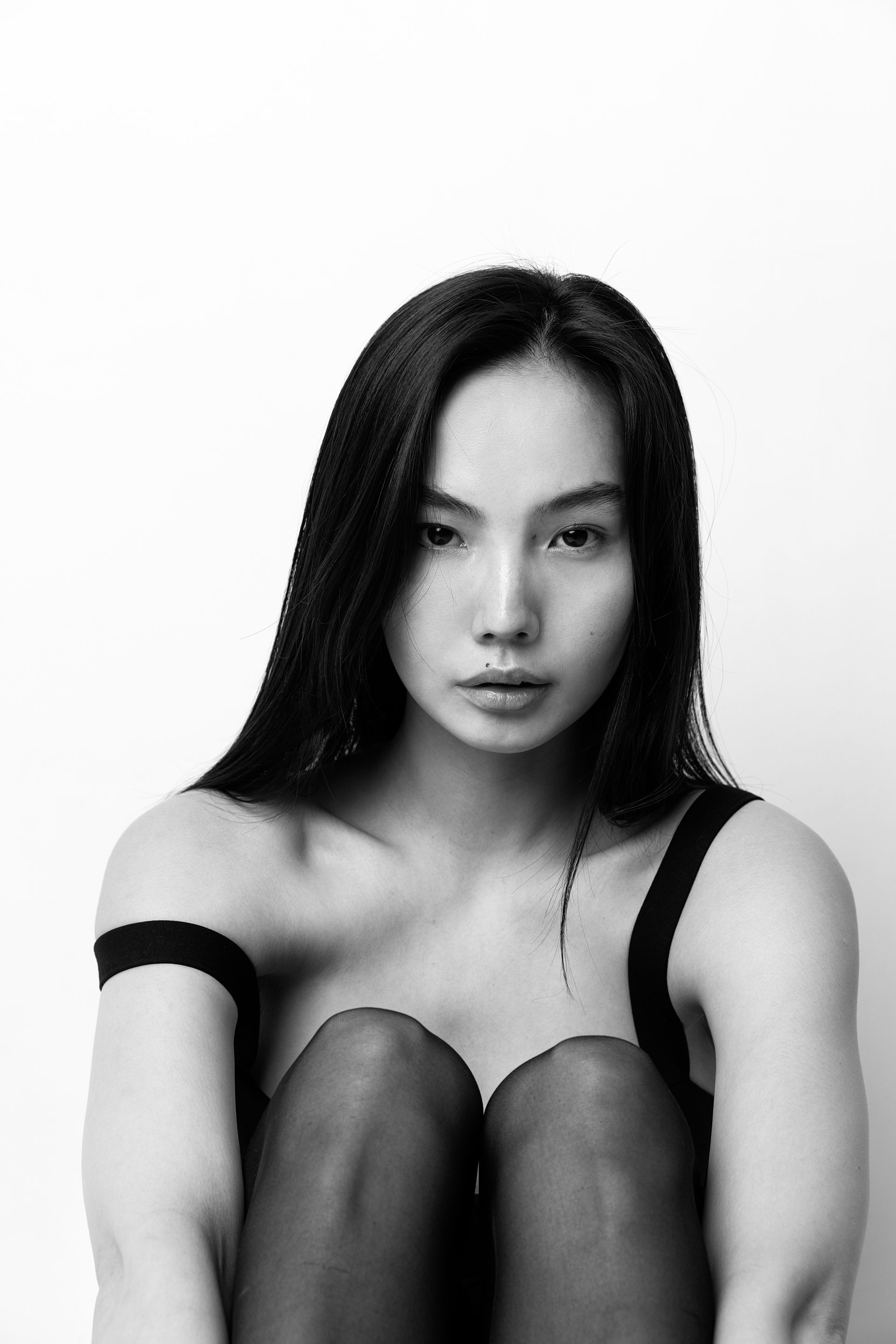 Woman in black tank top and tights looking at the camera, against a white backdrop.