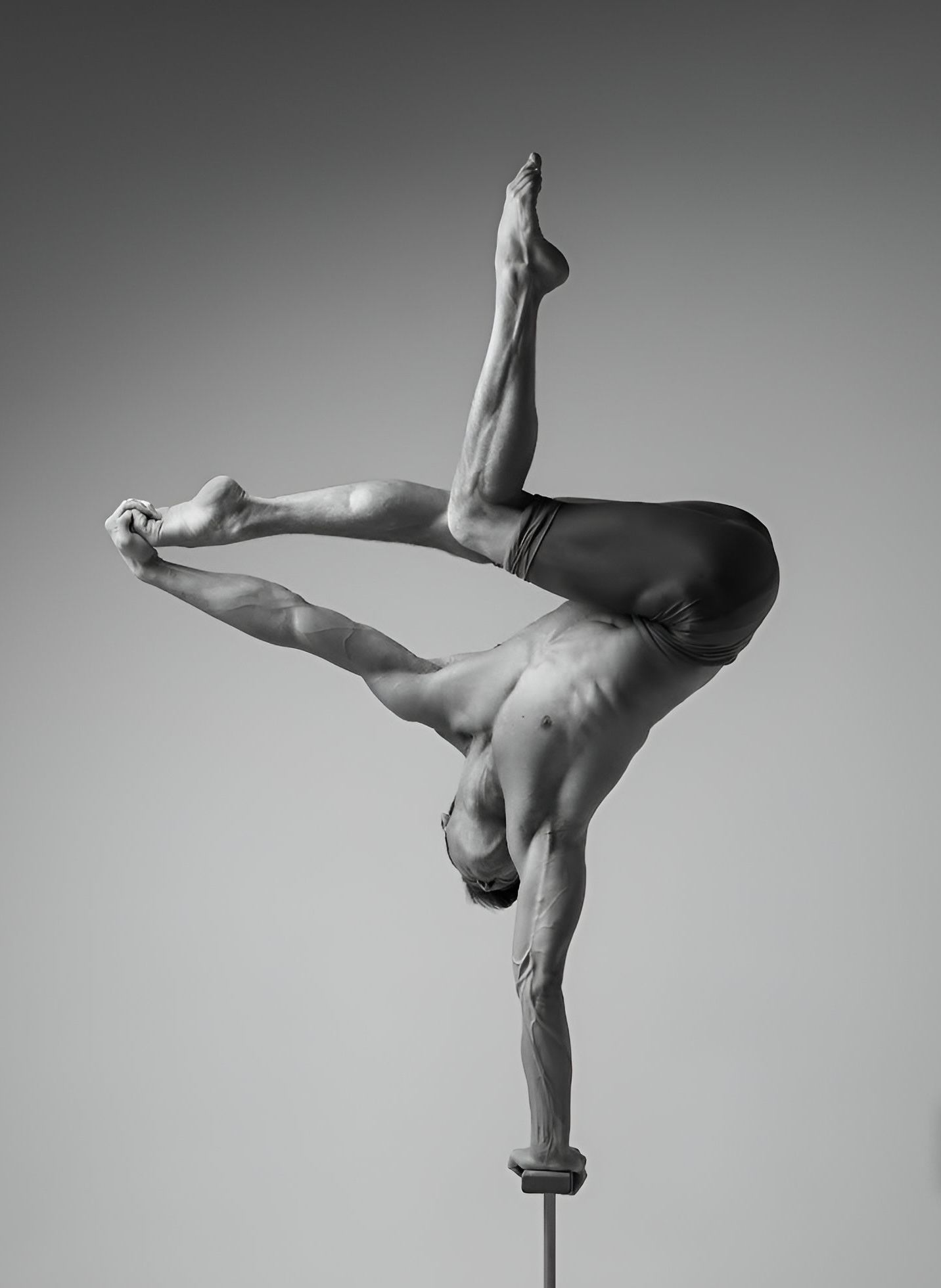 Acrobat balances on one hand, legs split above, body contorted, performing a gymnastic pose.