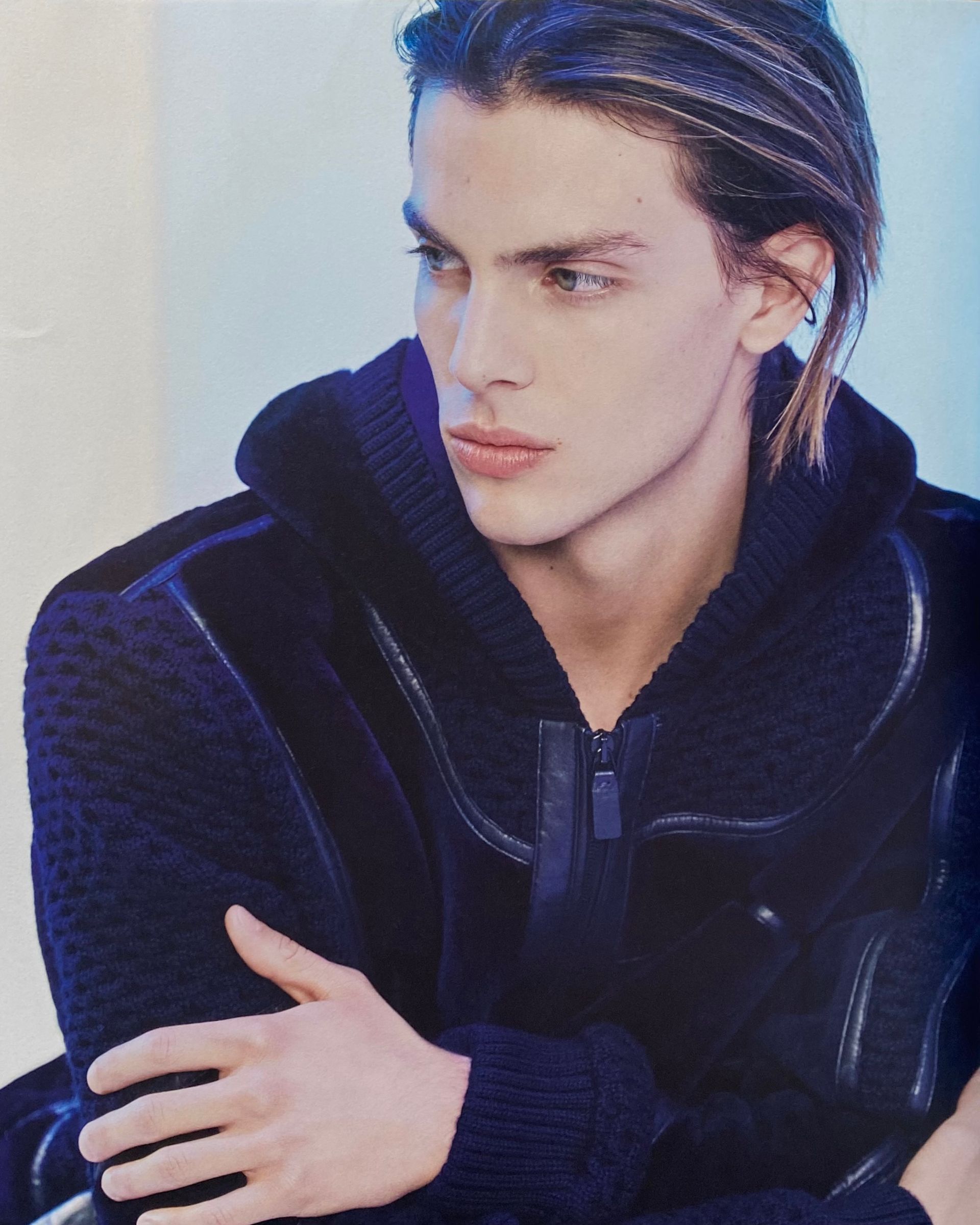 Man with slicked-back hair in a navy blue hooded sweater, looking off to the side with a pensive expression.