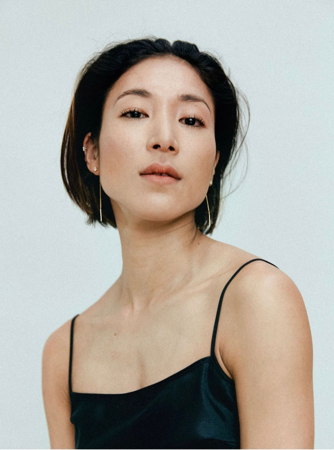 Woman in a dark spaghetti strap top, looking directly at the viewer, short dark hair, simple silver earrings.