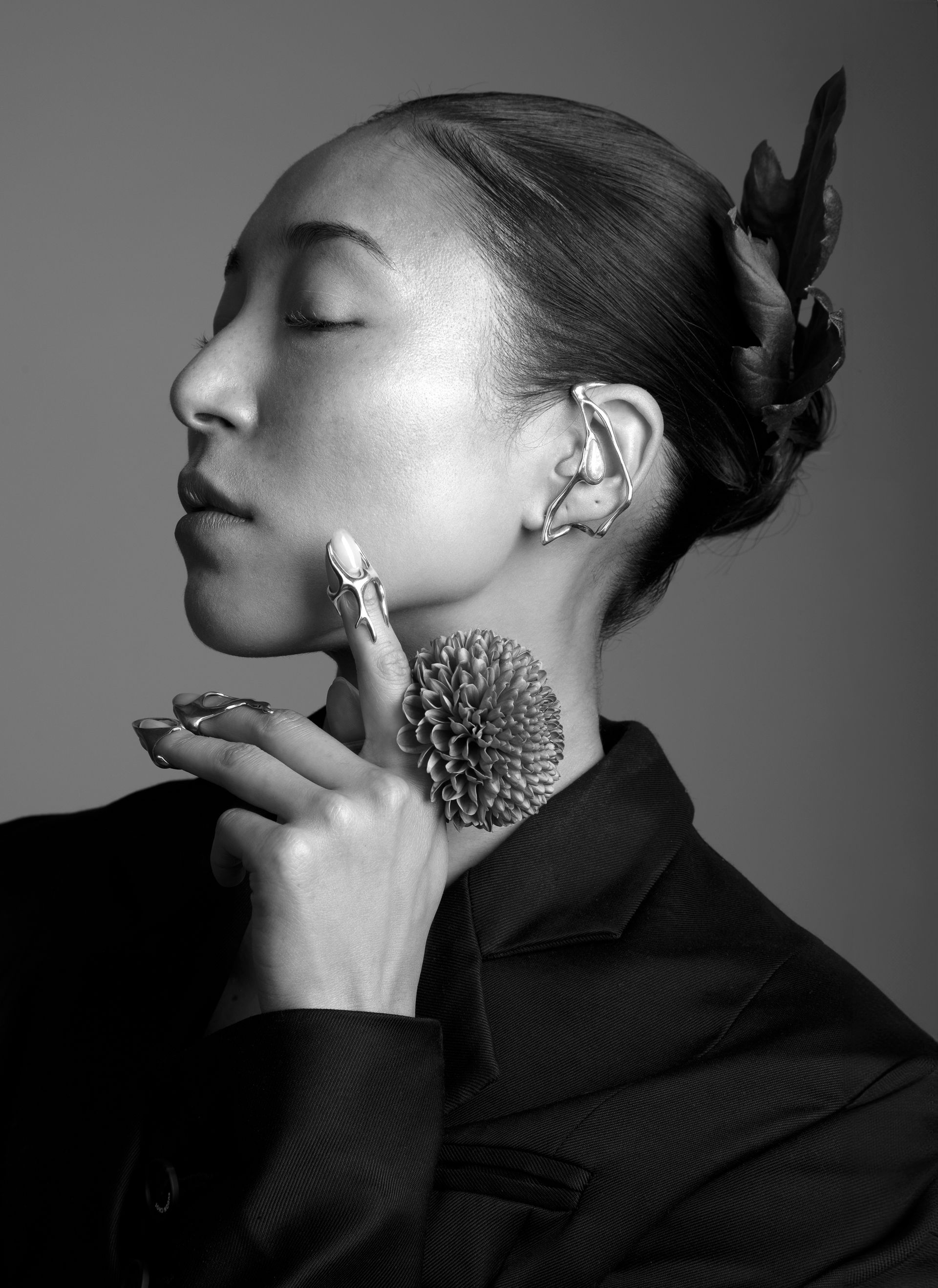 Woman wearing ear cuff and a ring, hand near neck, hair up. Black and white.