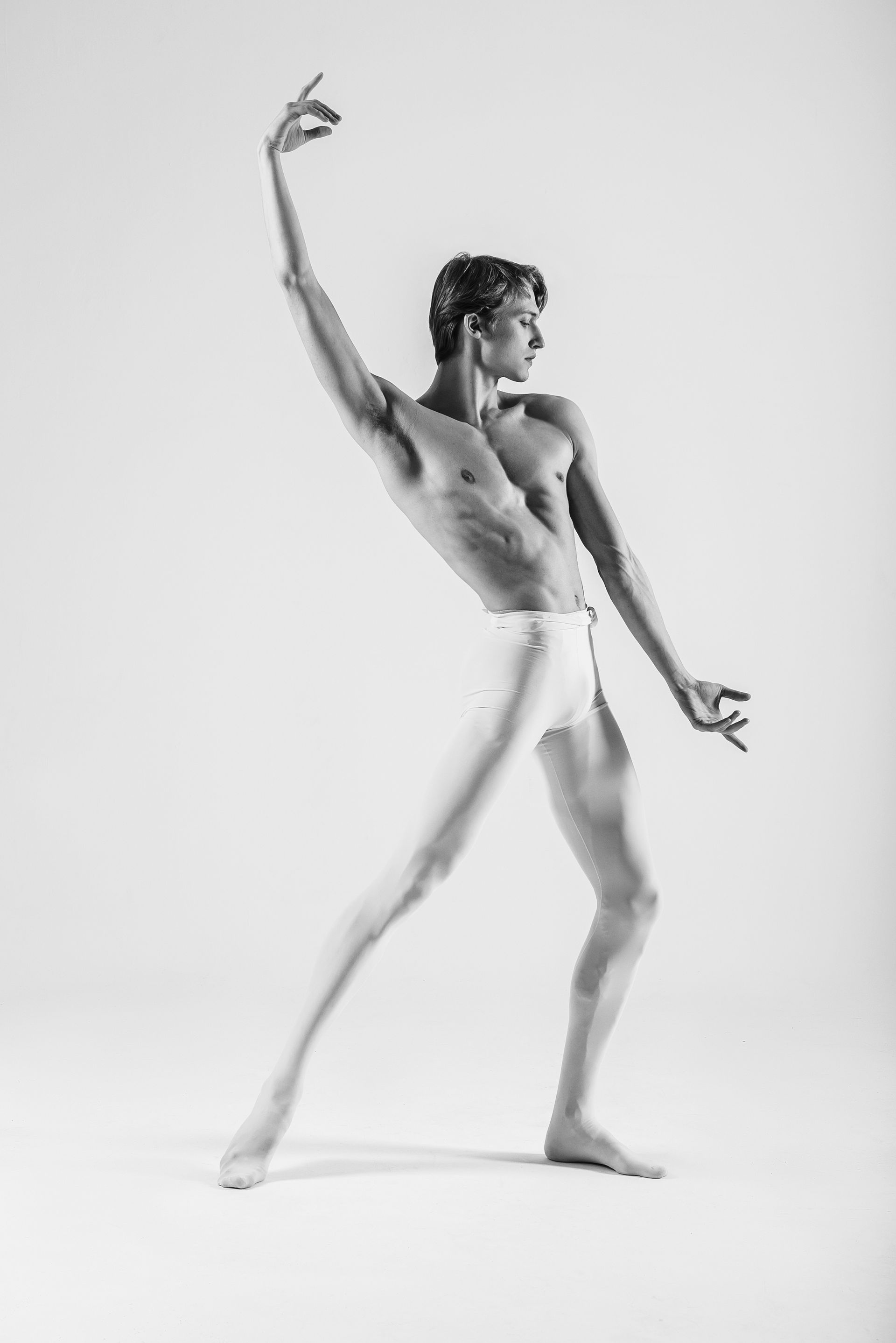 Male ballet dancer in white tights, barefoot, arms raised, poised, arched back.